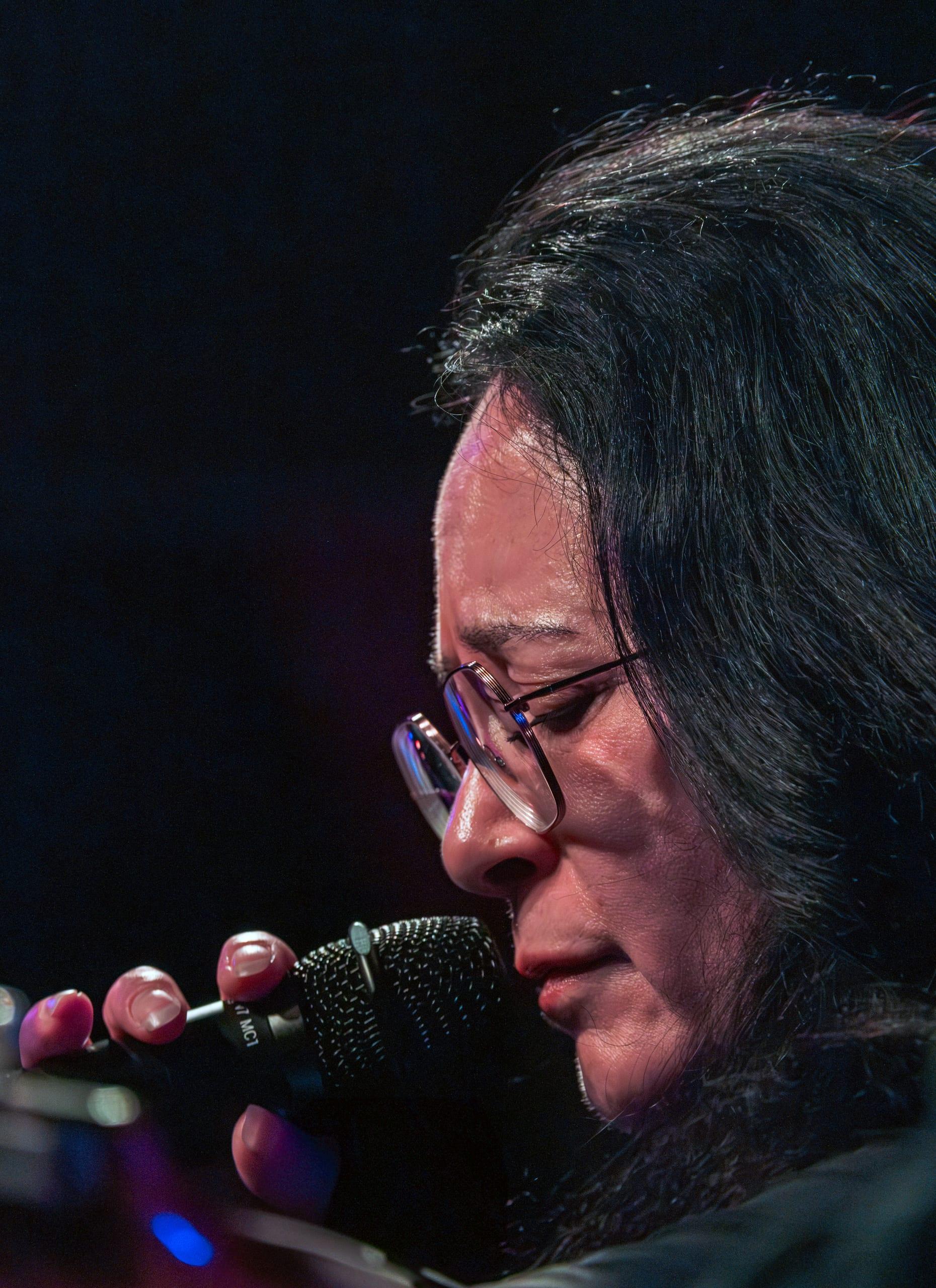 Singer with eyes closed, glasses catching the light, close at the microphone