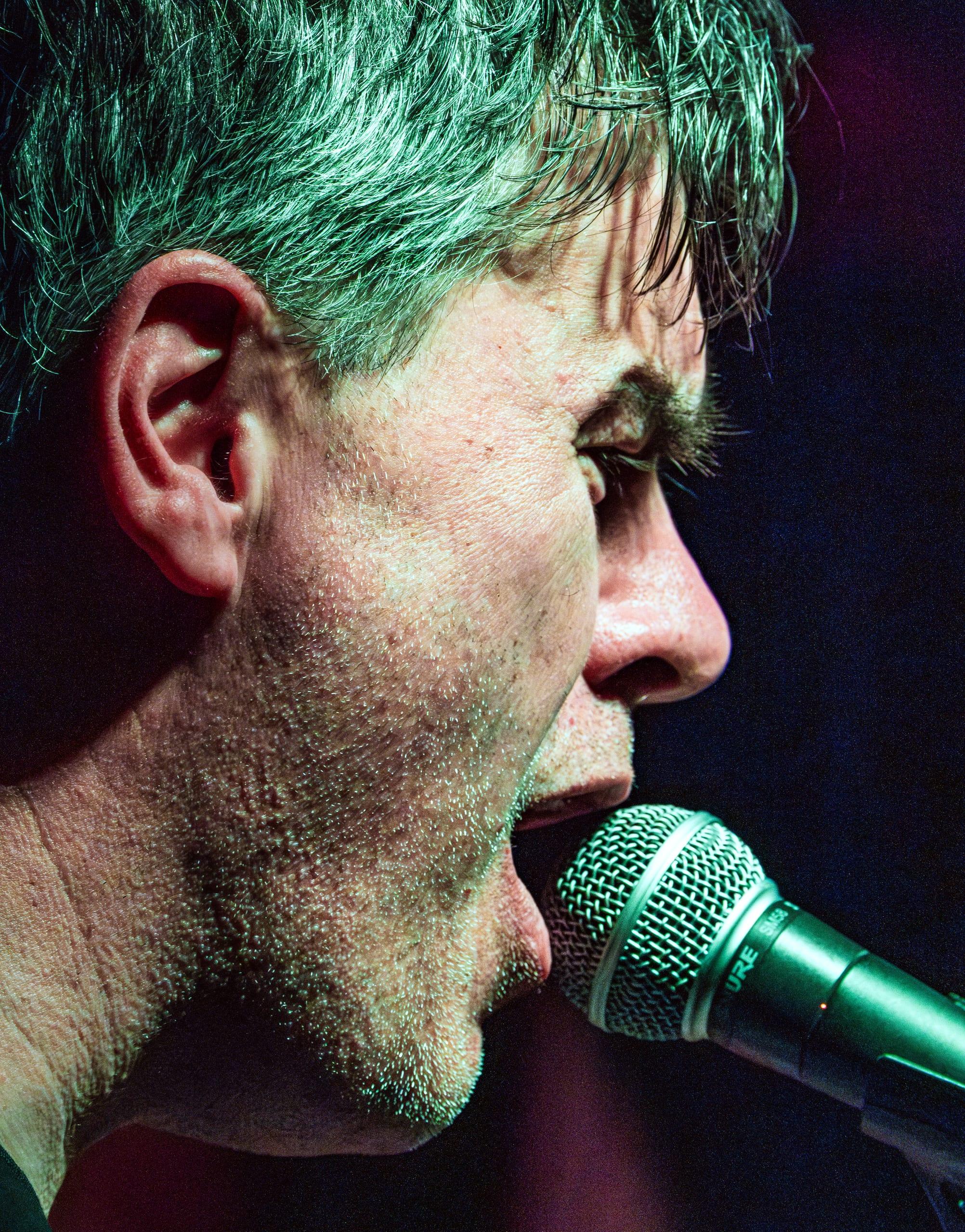 Singer in green stage light, close profile at the microphone