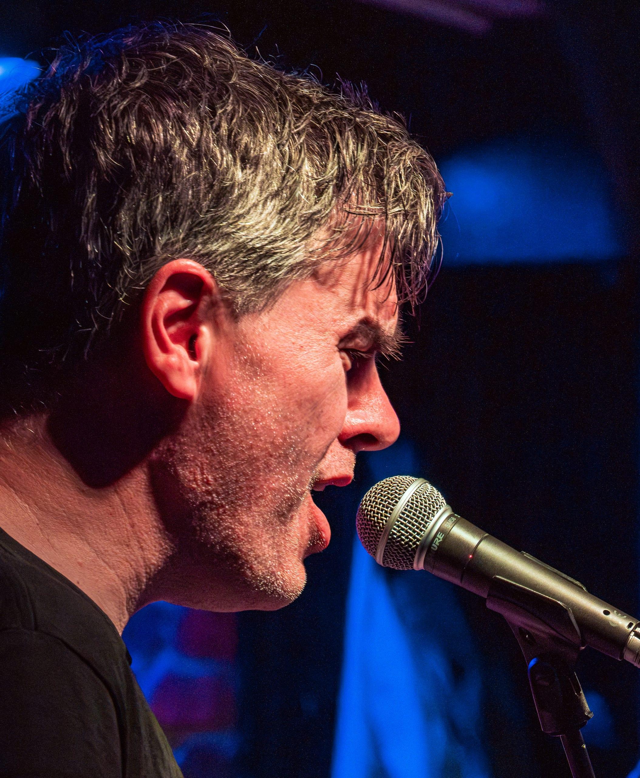 Extreme close profile of the singer at the microphone, sweat and stage light