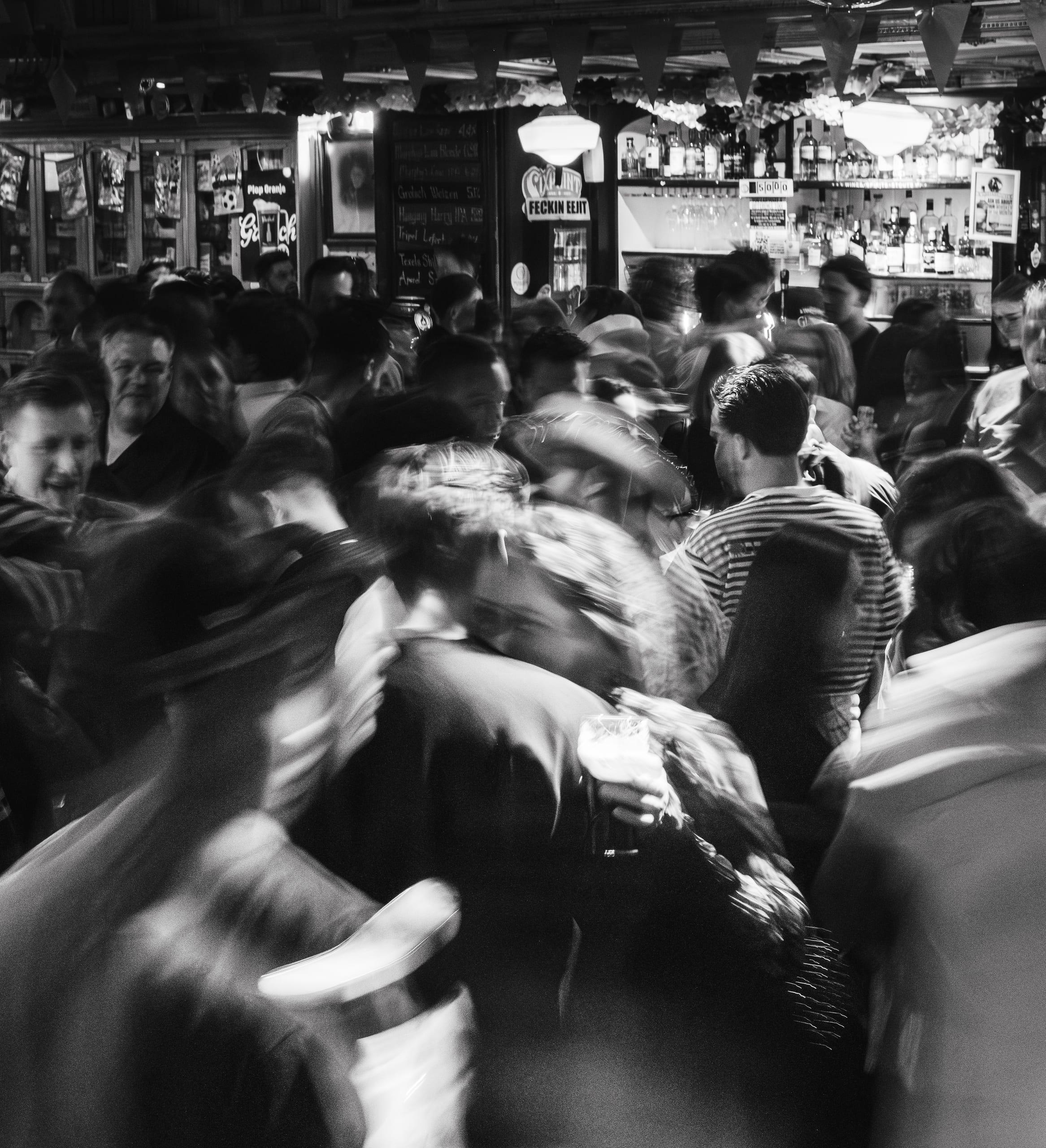 Black and white long exposure of a crowd dancing near the bar, motion-blurred