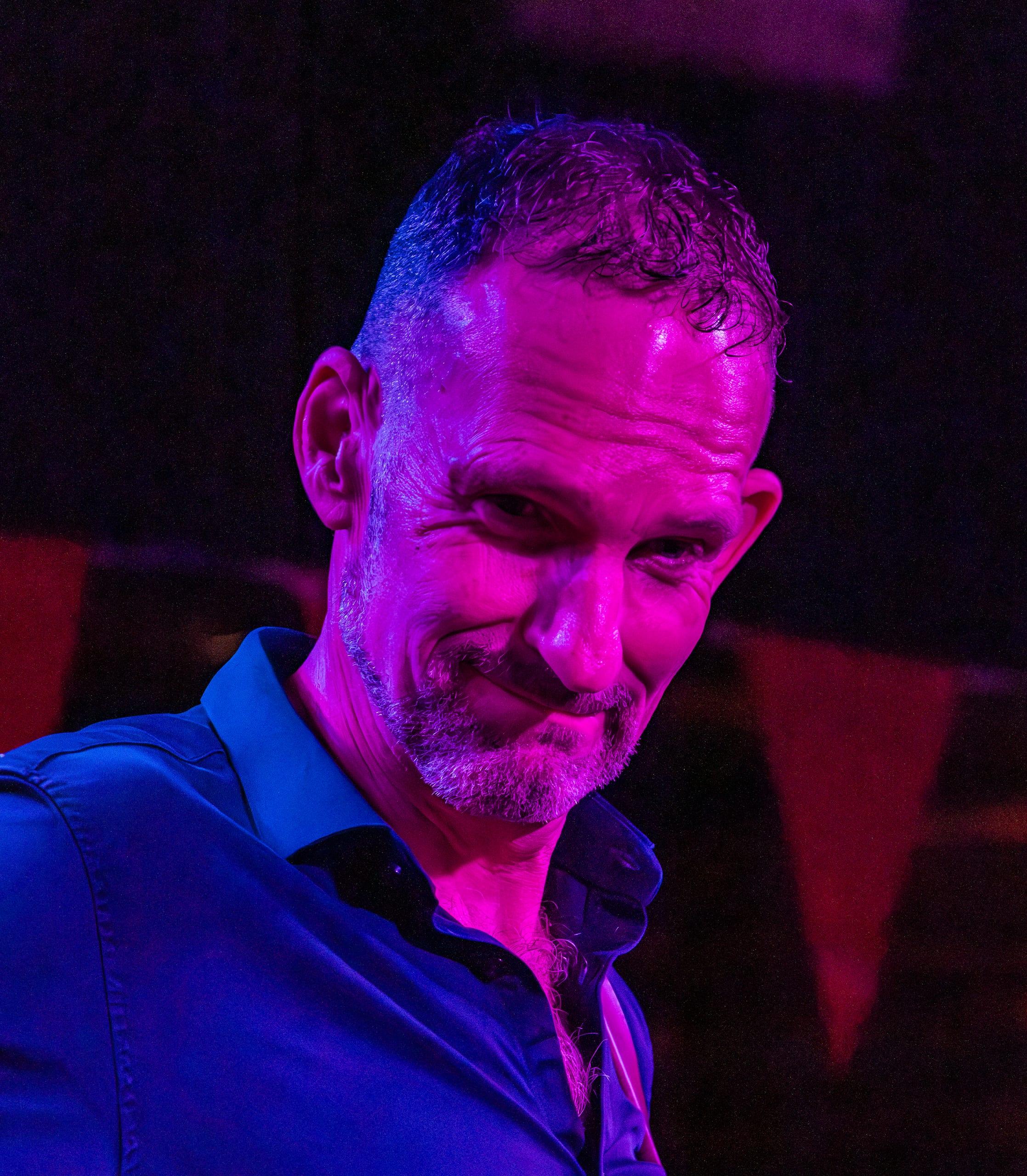 Close portrait of a man smirking under pink and blue stage light