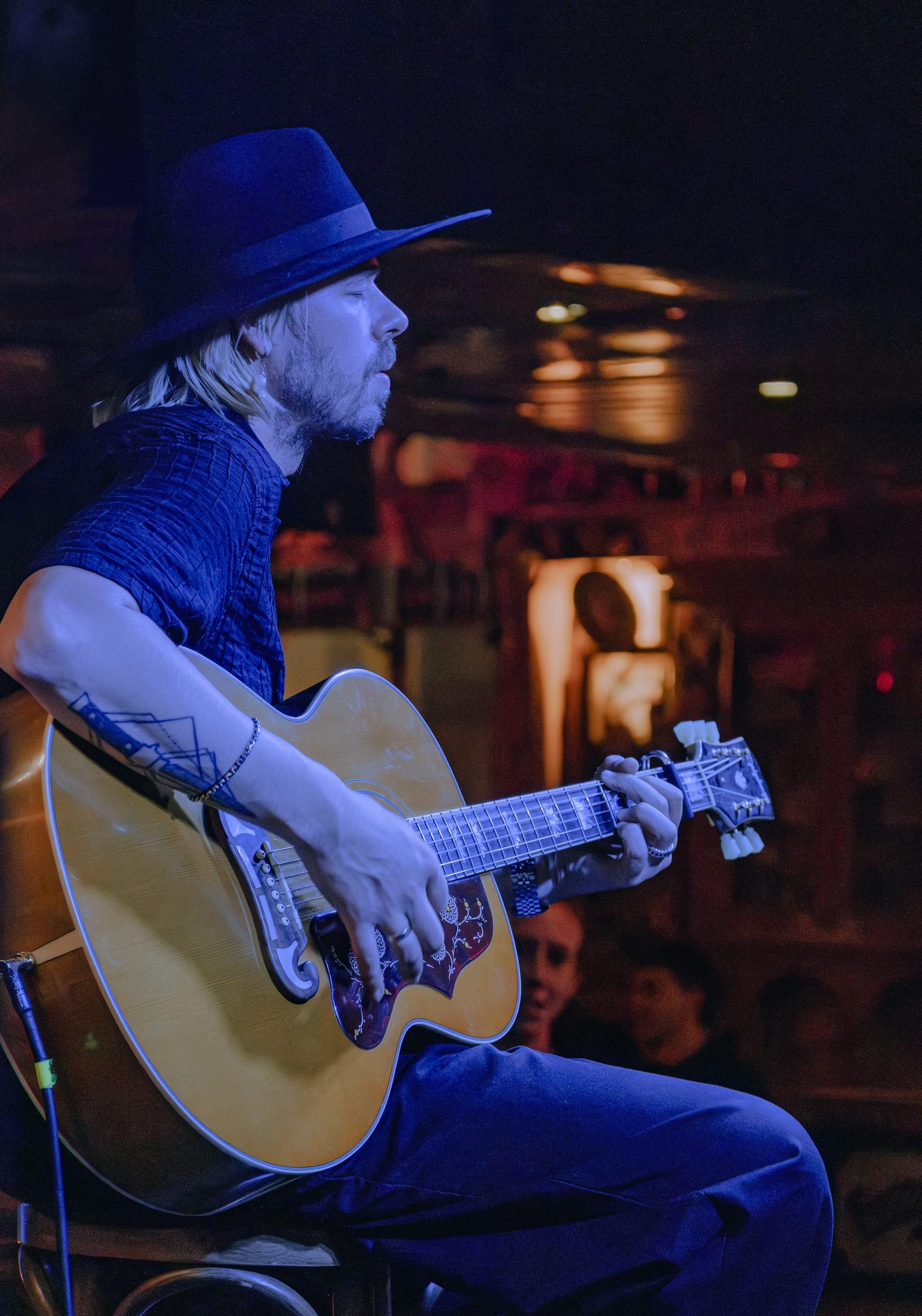 Guitarist in profile playing an acoustic guitar under blue stage light