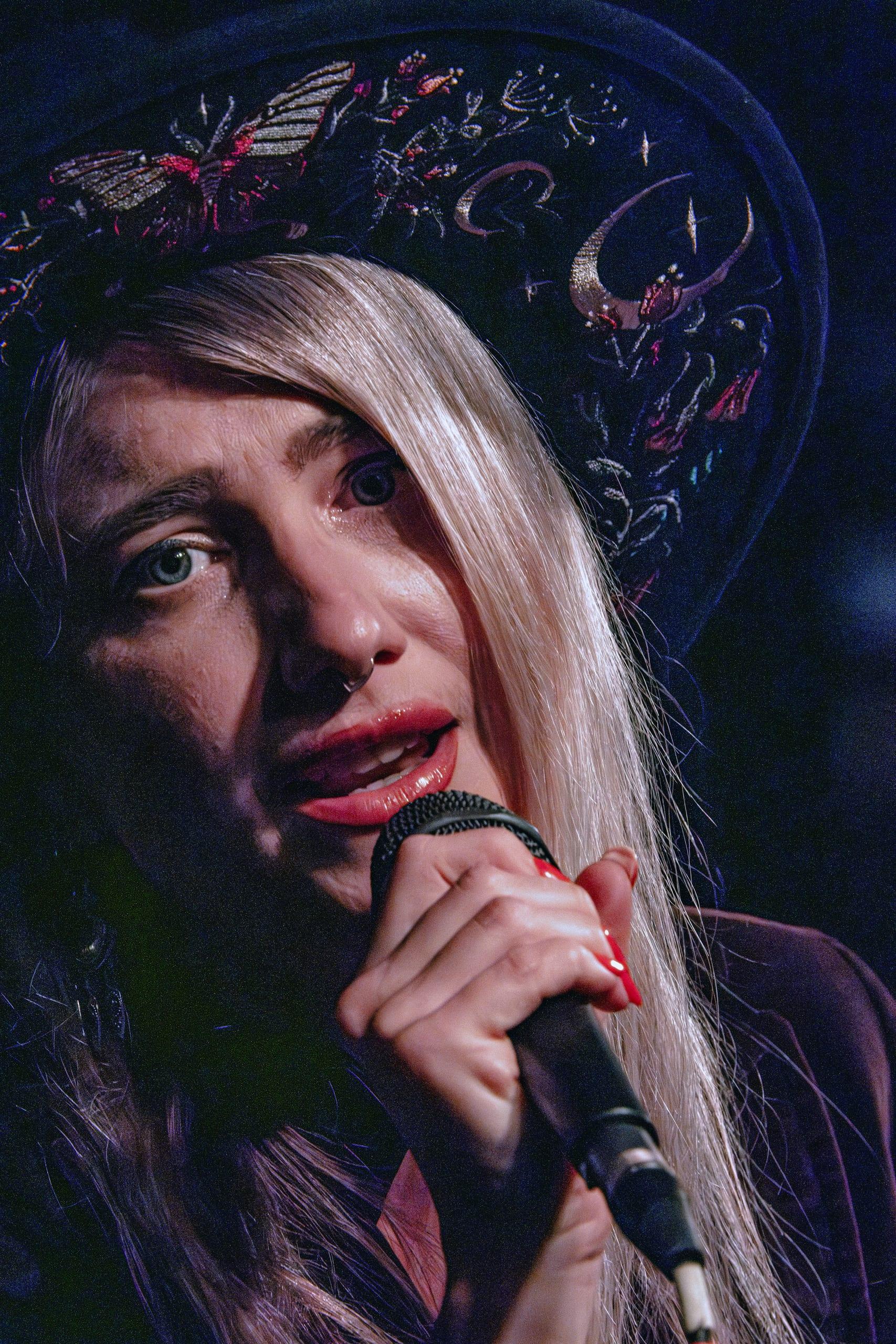 Guitarist's face lit entirely in red beneath a wide-brimmed hat