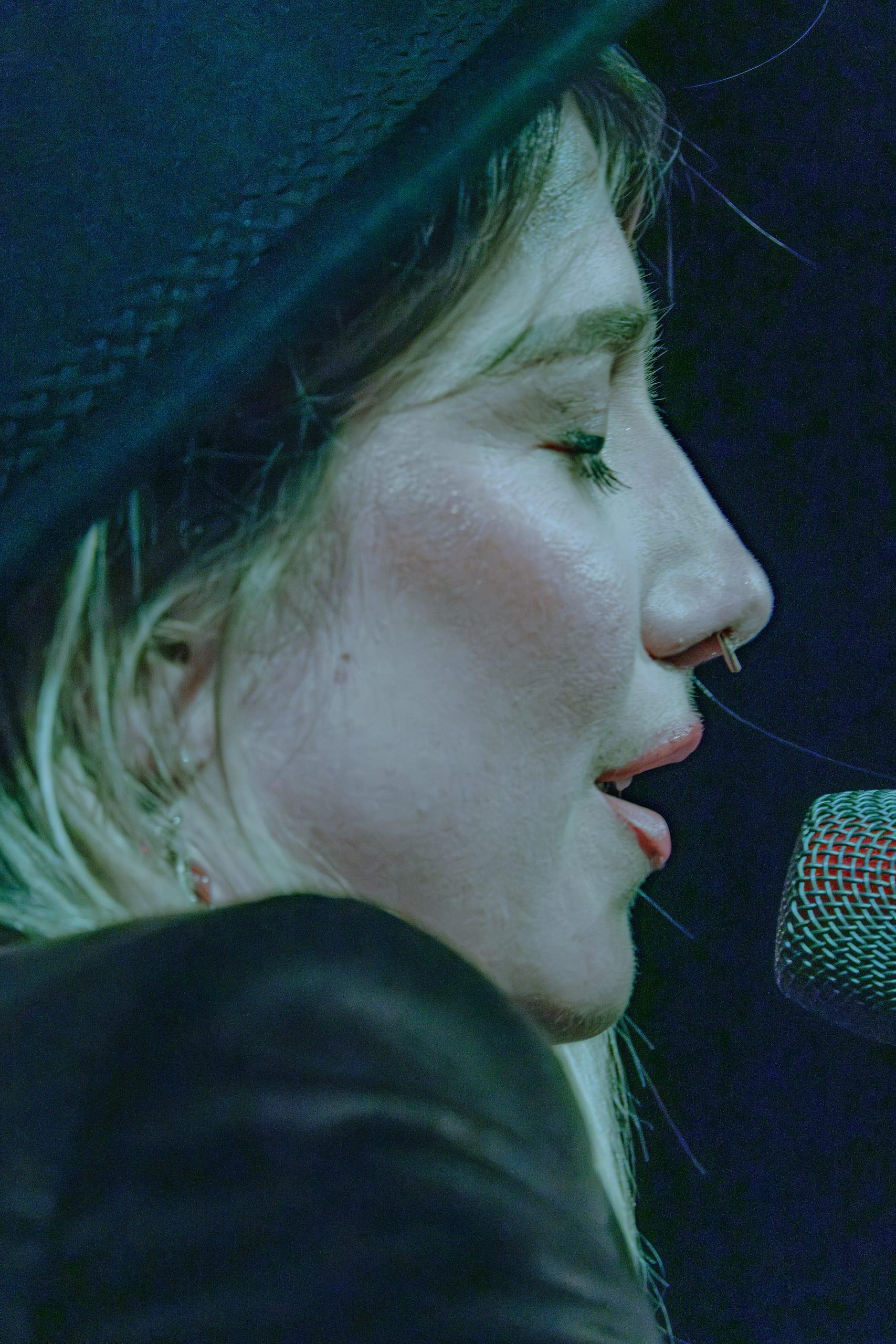 Extreme close profile of the singer mid-note, teal stage light