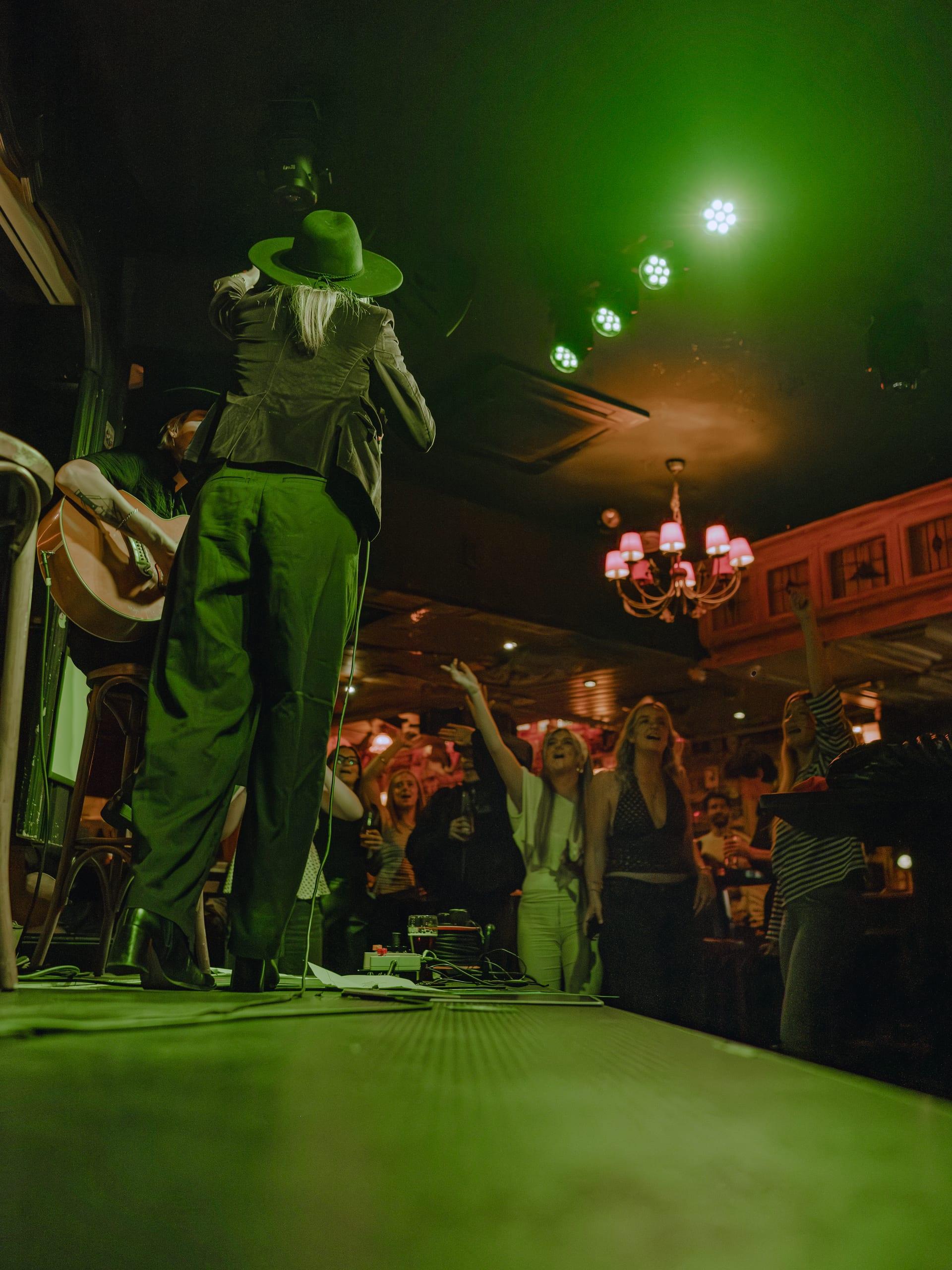 Wide shot from the stage of the crowd with arms raised, green stage light, chandelier glowing red