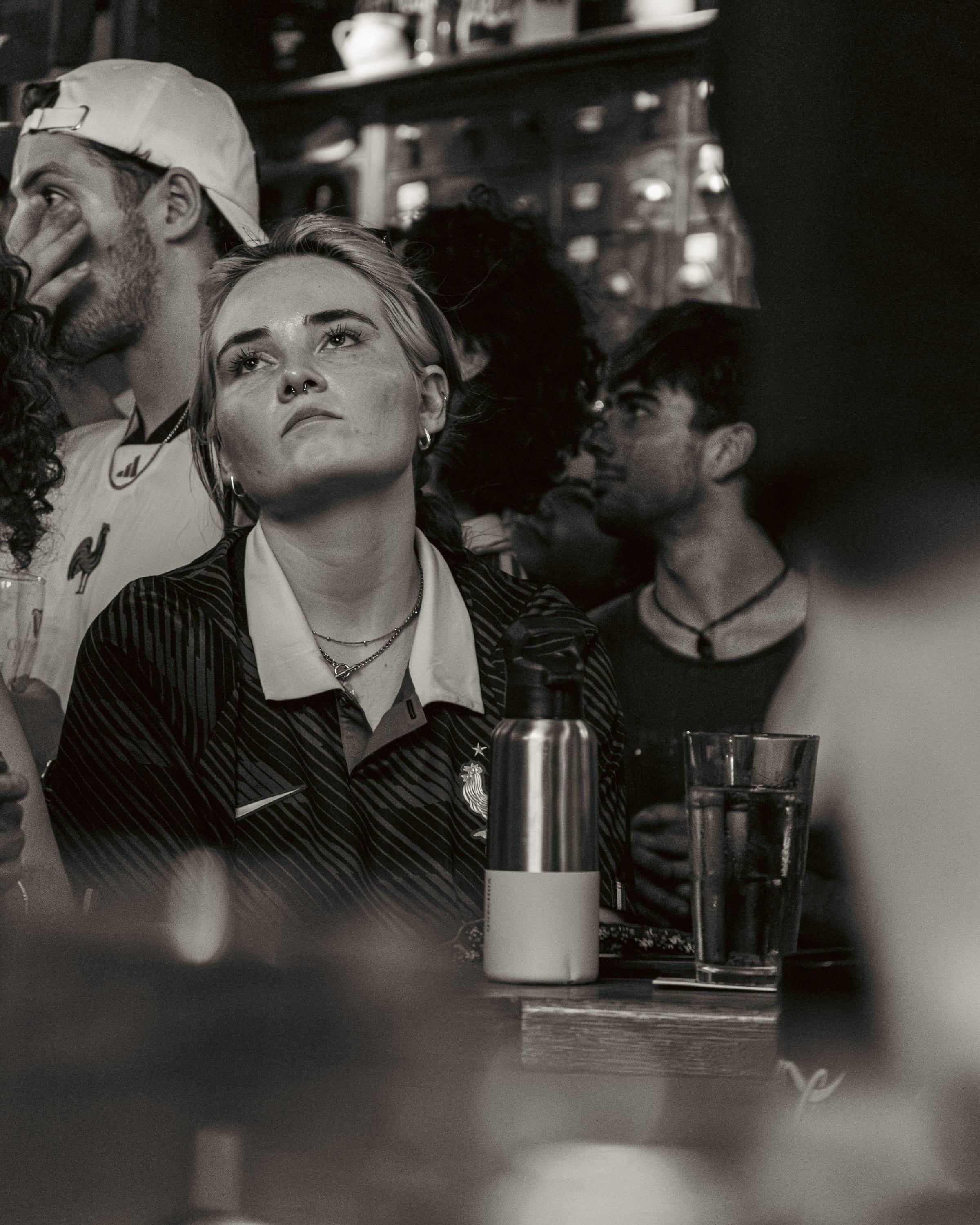 Black-and-white portrait of a fan in a vintage France shirt, a friend beside her hand over his mouth