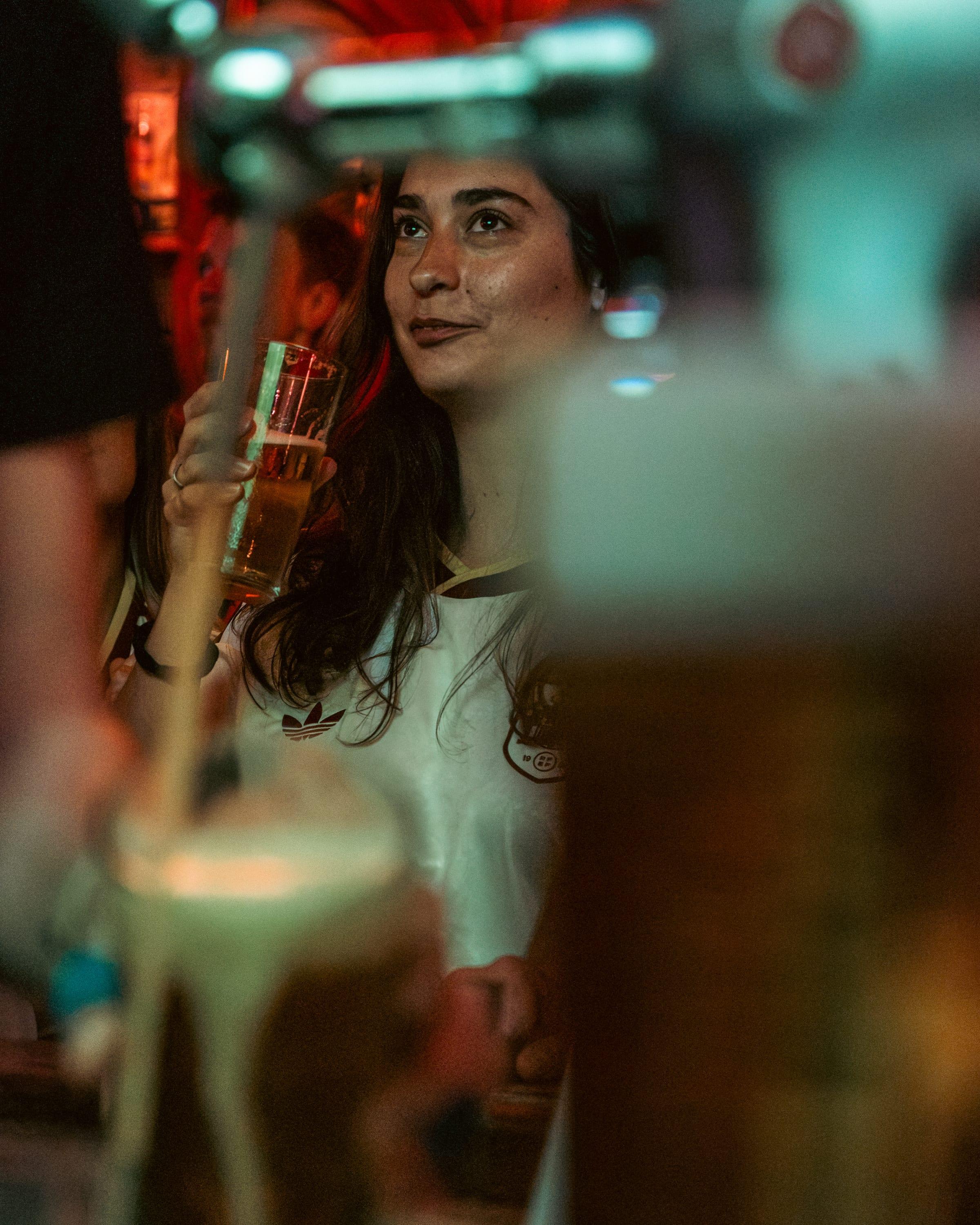 Fan mid-sip in an Adidas shirt, pint raised, eyes on the match