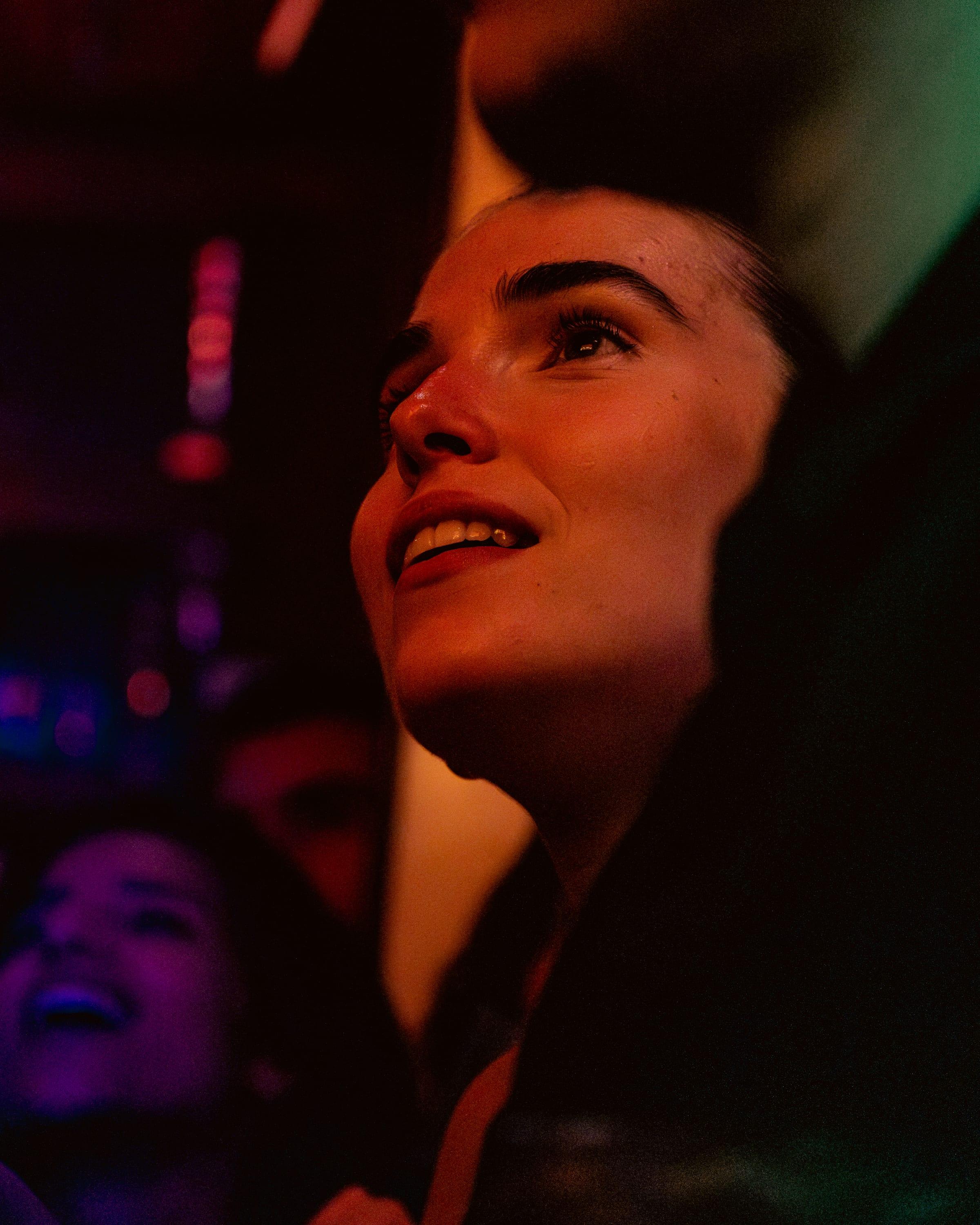 Close portrait of a fan smiling up at the screen, lit warm and red