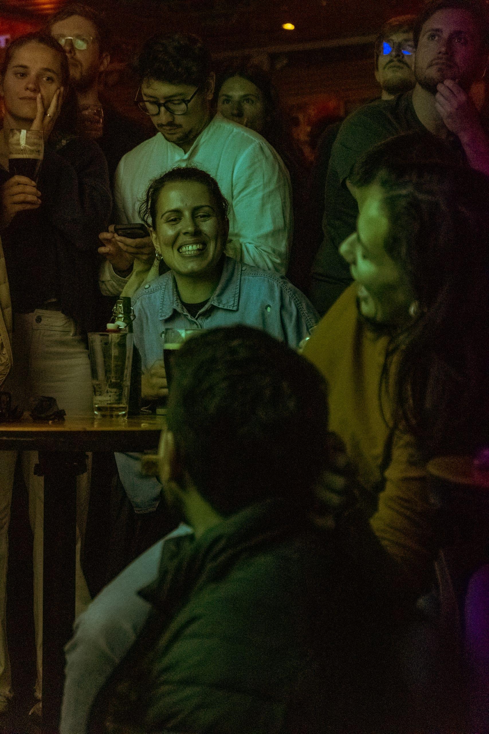 Fan laughing with friends at a packed table, phone raised
