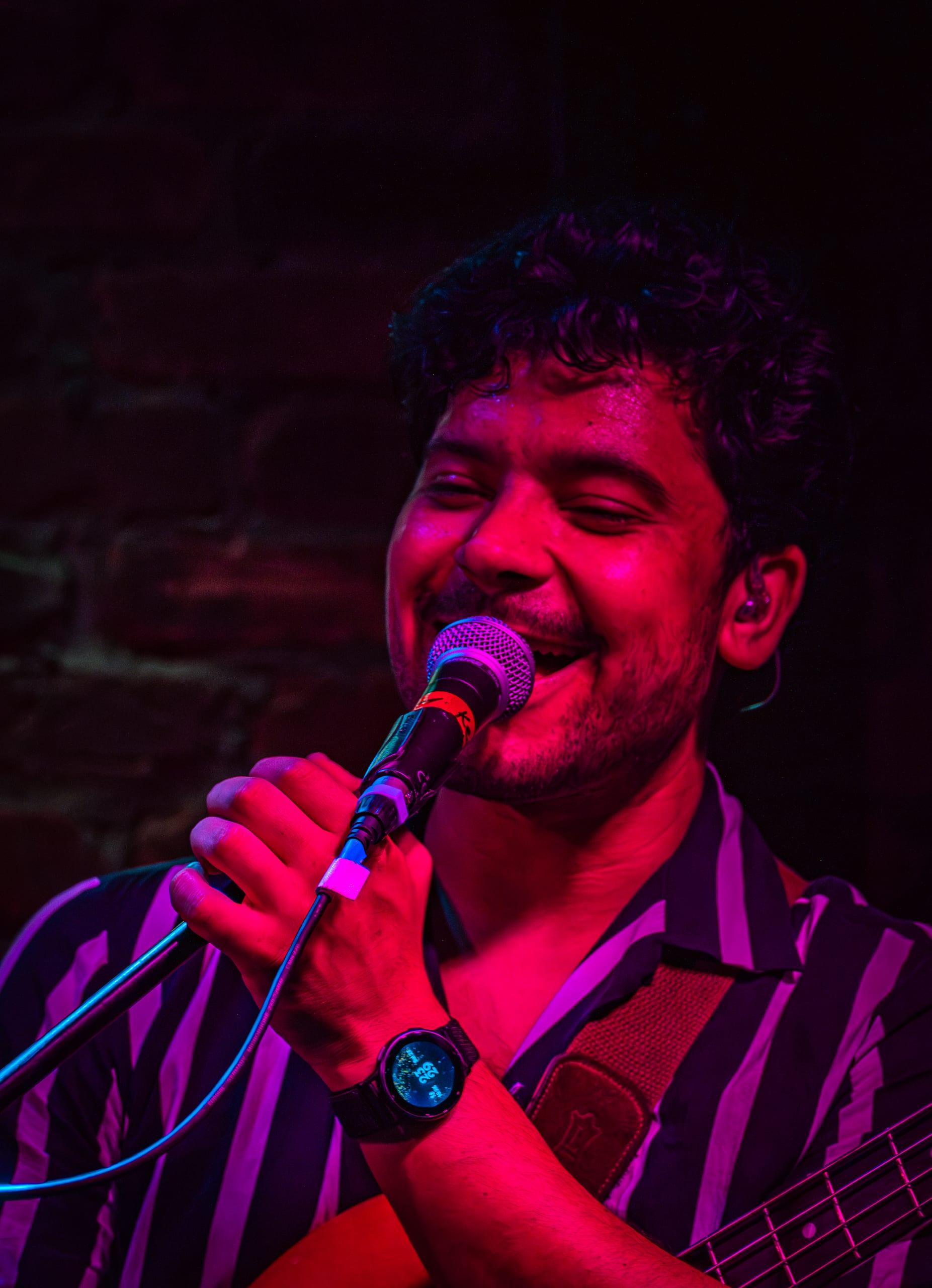 Vocalist singing with eyes closed under magenta stage light, full voice, full commitment