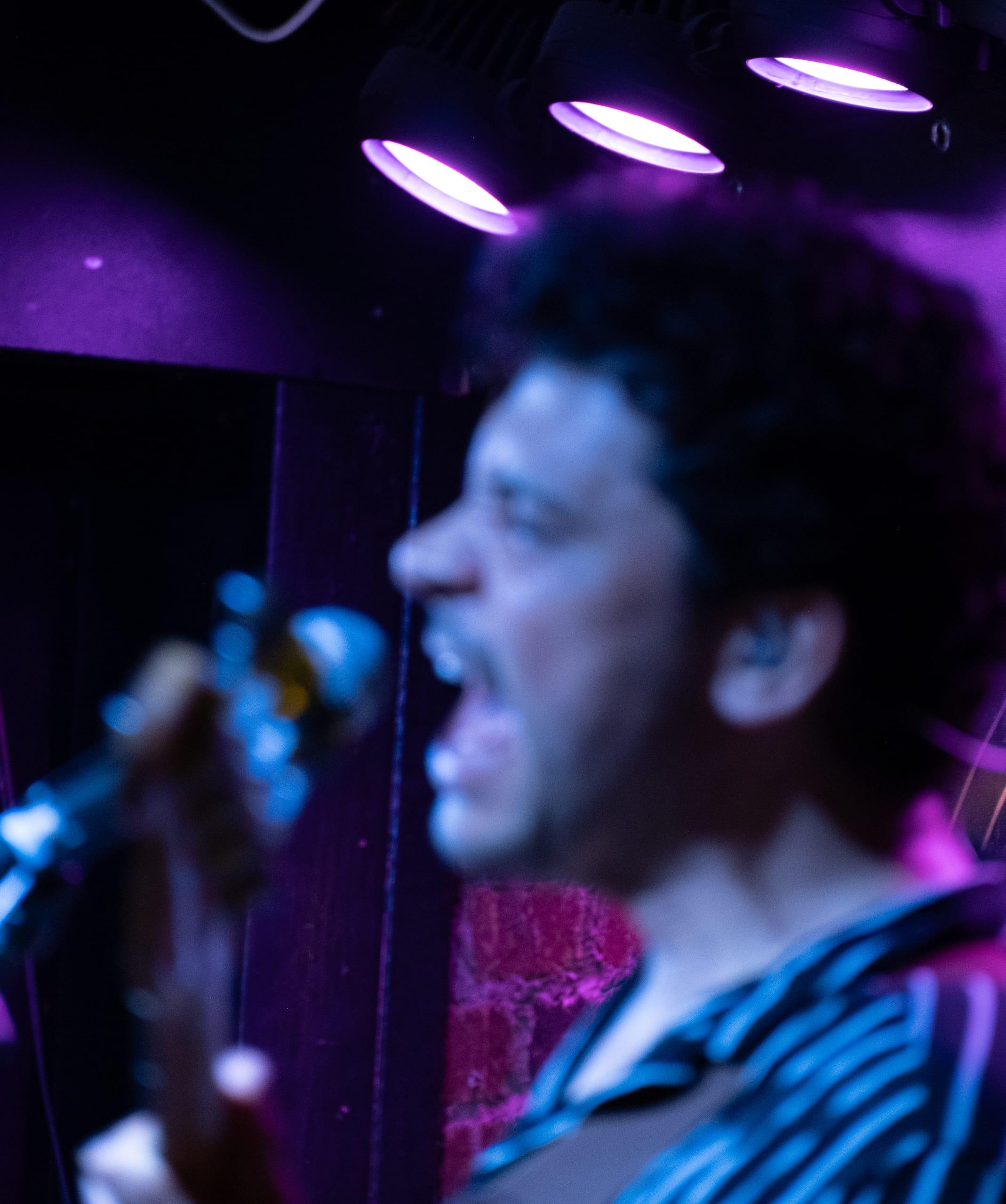 Long exposure blur of a singer's profile in motion, purple and blue stage light trailing