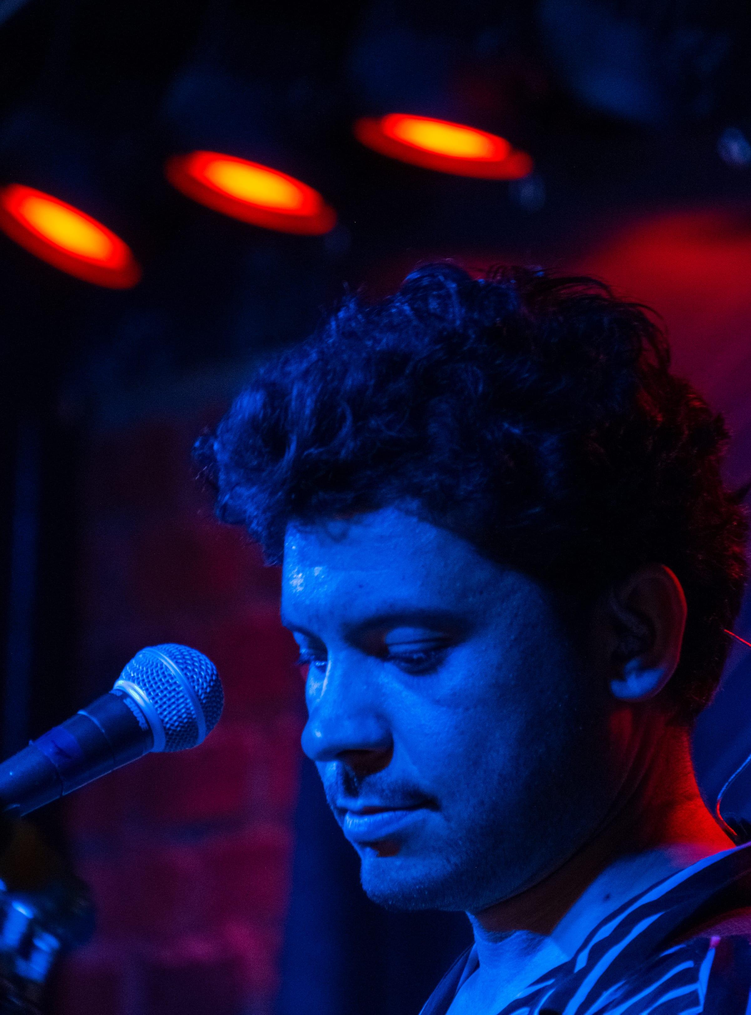 Close portrait under blue light, eyes lowered toward the mic, curls damp with the set's heat