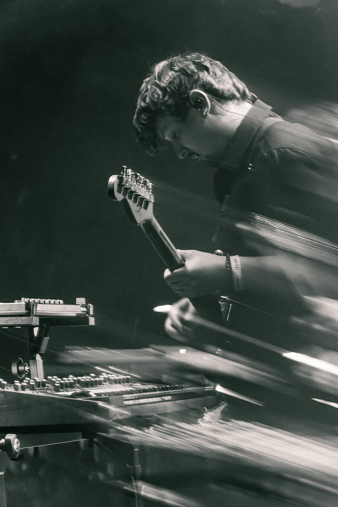 Long exposure black-and-white photo of a guitarist mid-performance, motion blurring the stage lights around him
