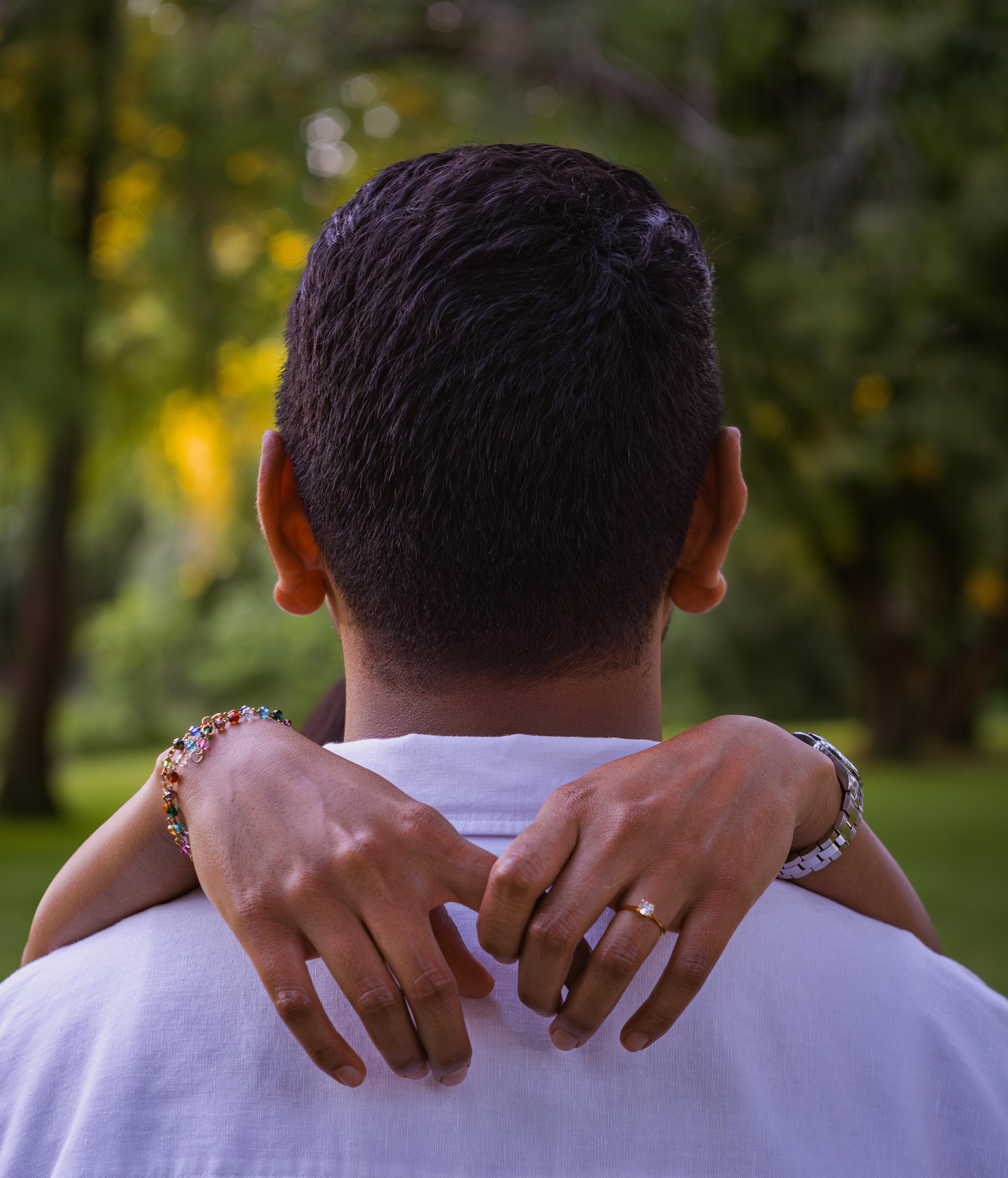 Couple embracing outdoors at golden hour, hands clasped behind his neck