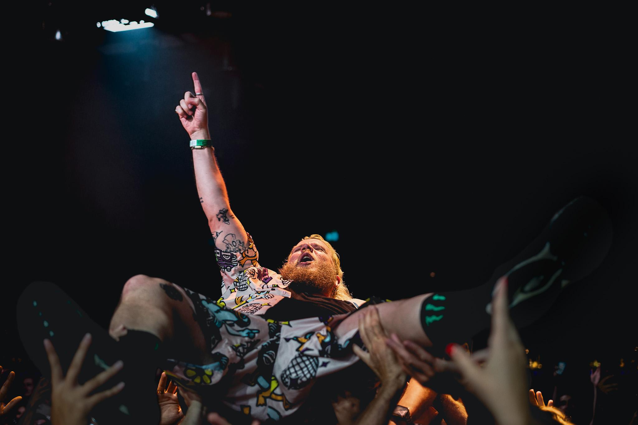 A fan lifted overhead by the crowd, arm raised, lit by a single spotlight beam