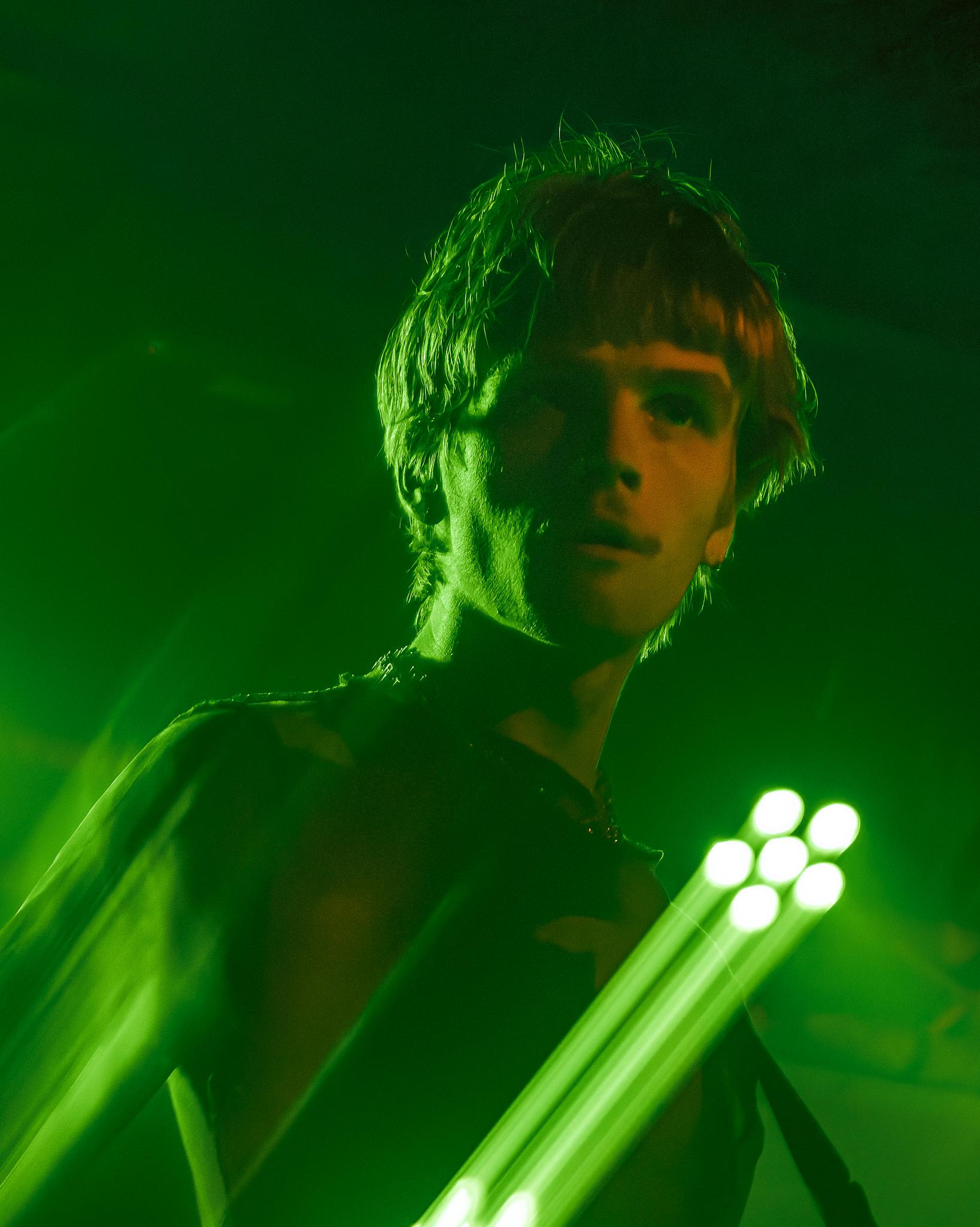 A musician gripping a light fixture, looking toward camera