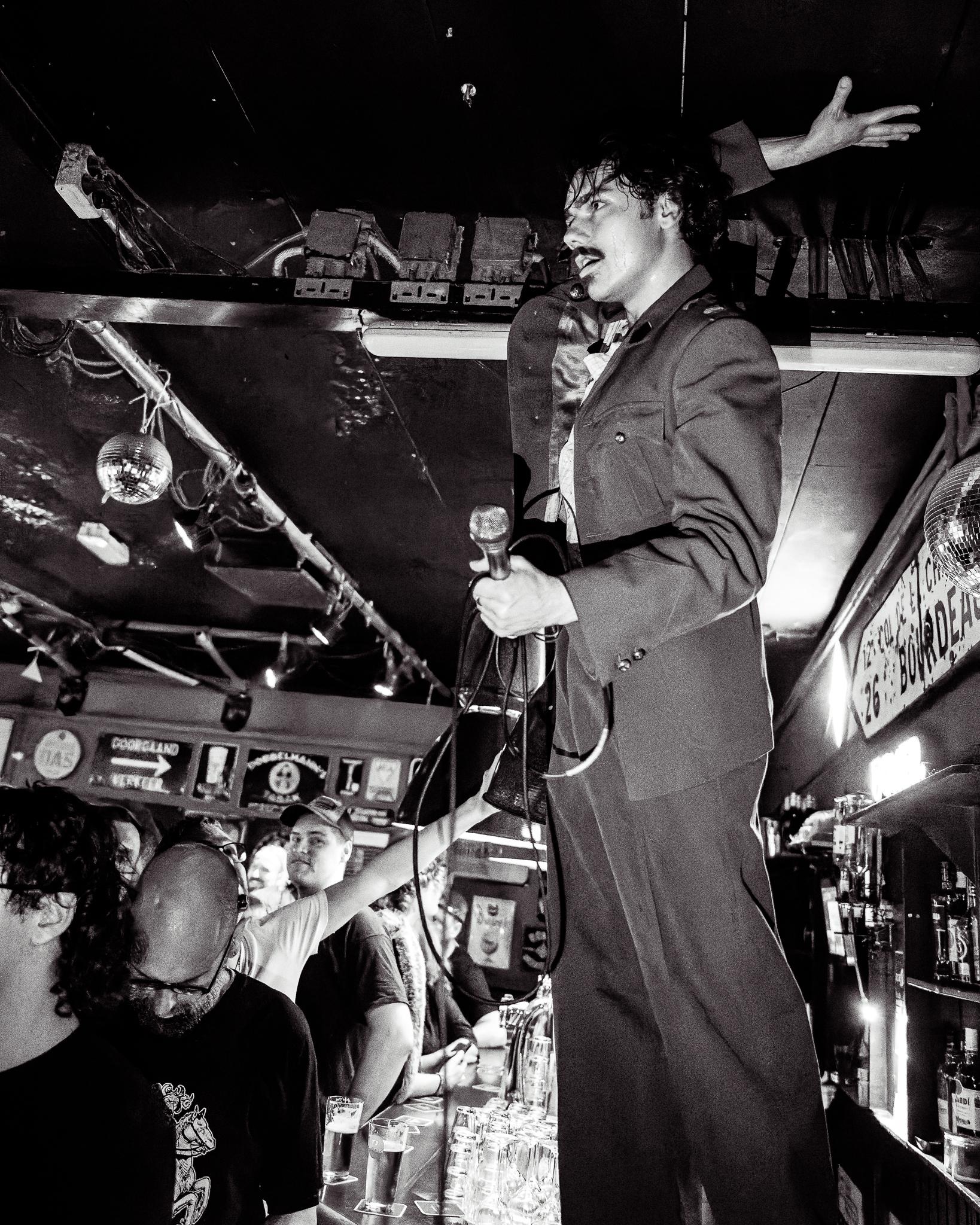 A singer standing on the bar mid-performance, arm raised, disco ball catching the light, black and white
