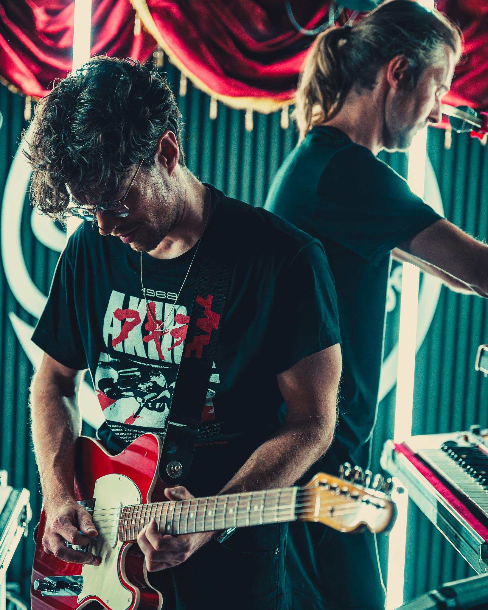 Two guitarists mid-performance, one in an AKIRA t-shirt