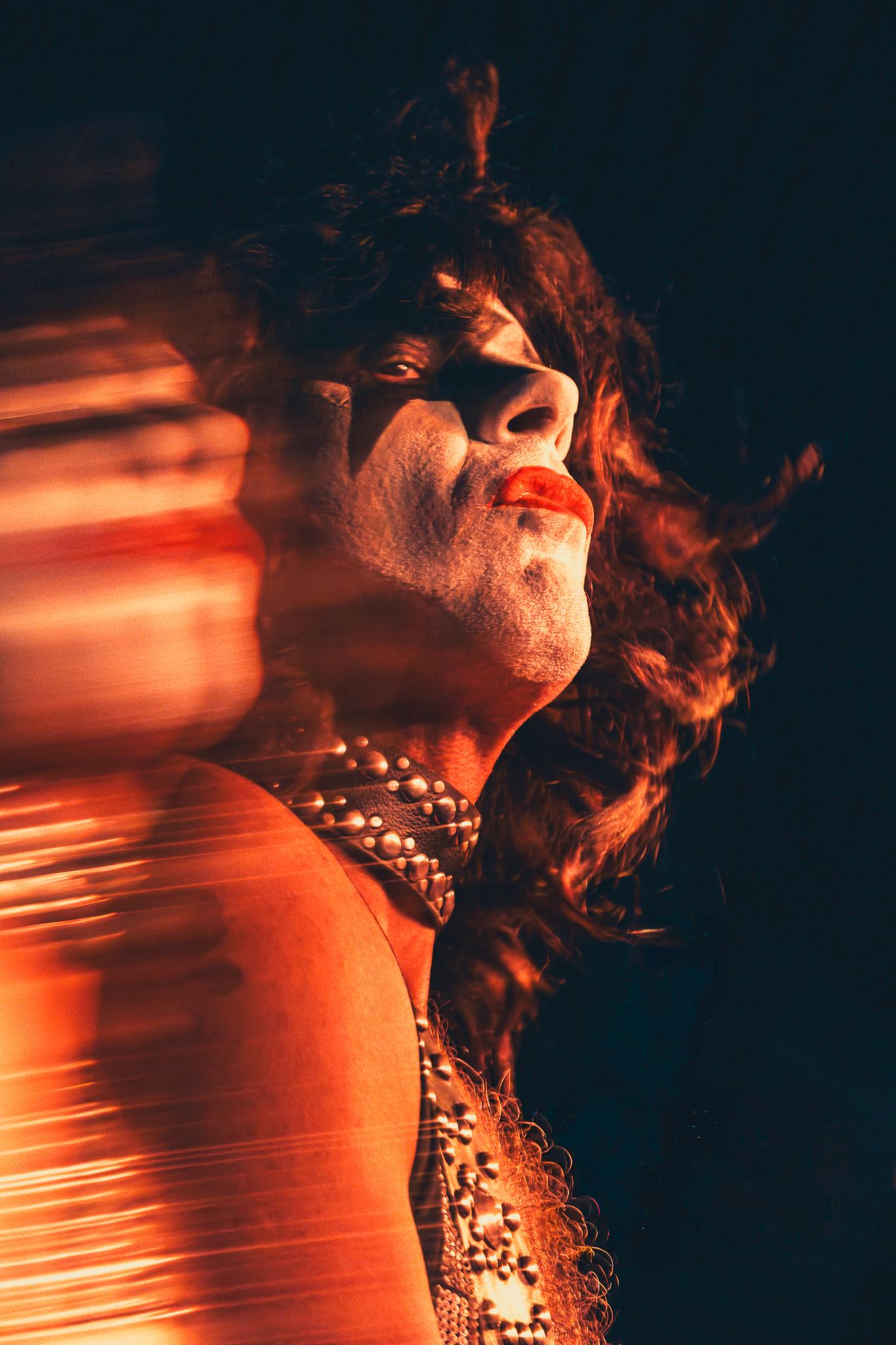 A KISS-style face-painted performer caught in motion blur under red light
