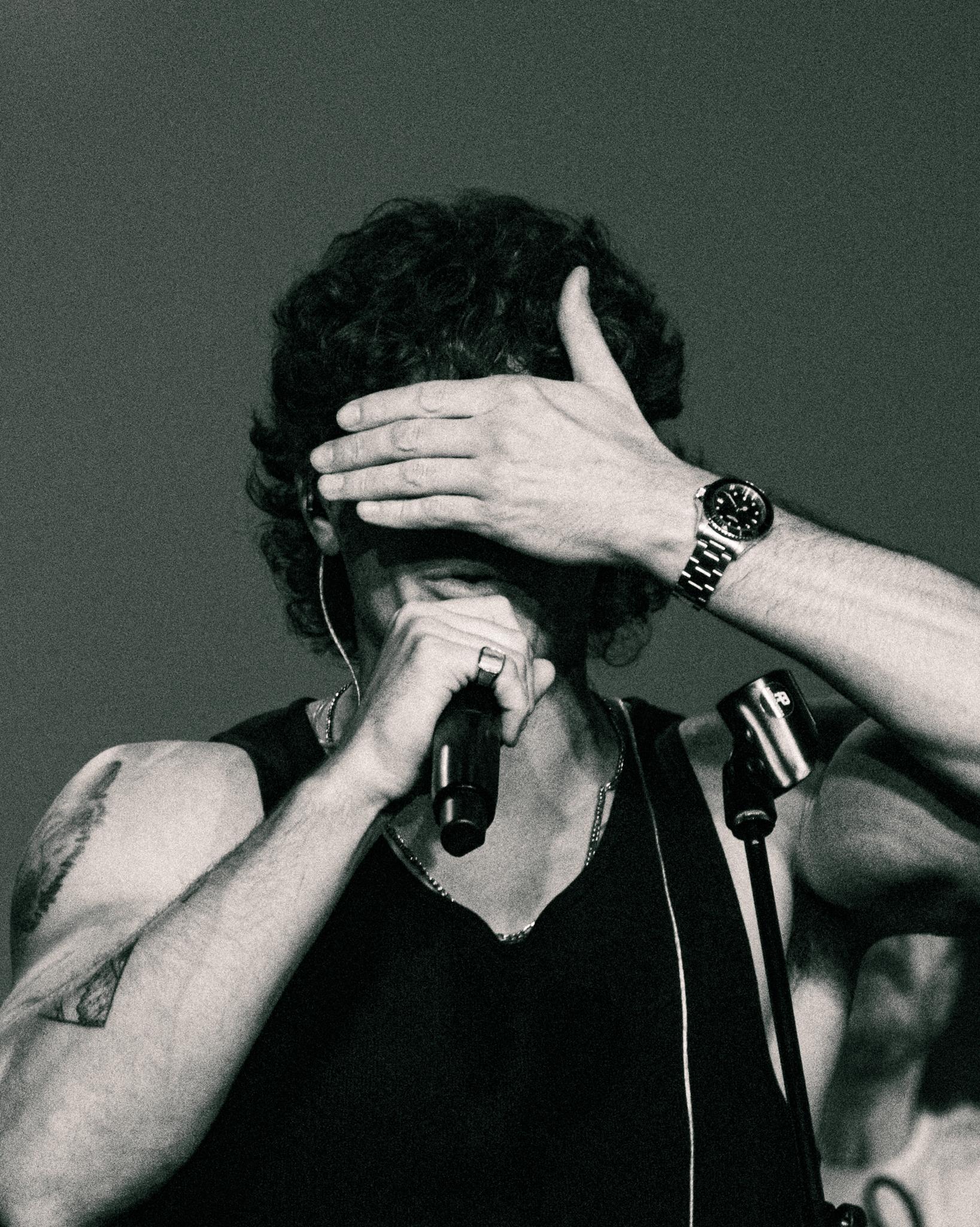 A singer shielding his eyes mid-note, hand raised to his face, microphone close