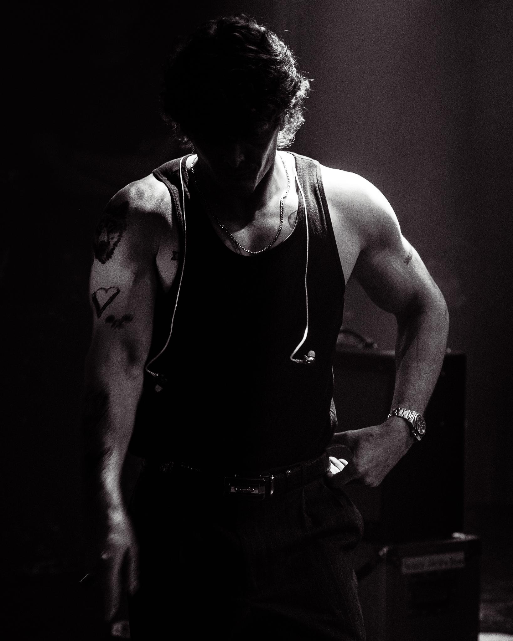 A silhouetted musician flexing between songs, chain and earpiece catching the light, black and white