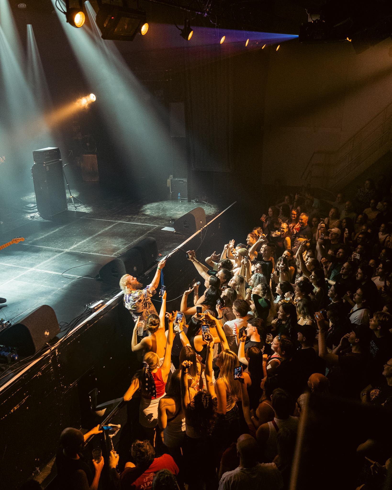 A singer reaching down into the crowd from the stage, seen from above
