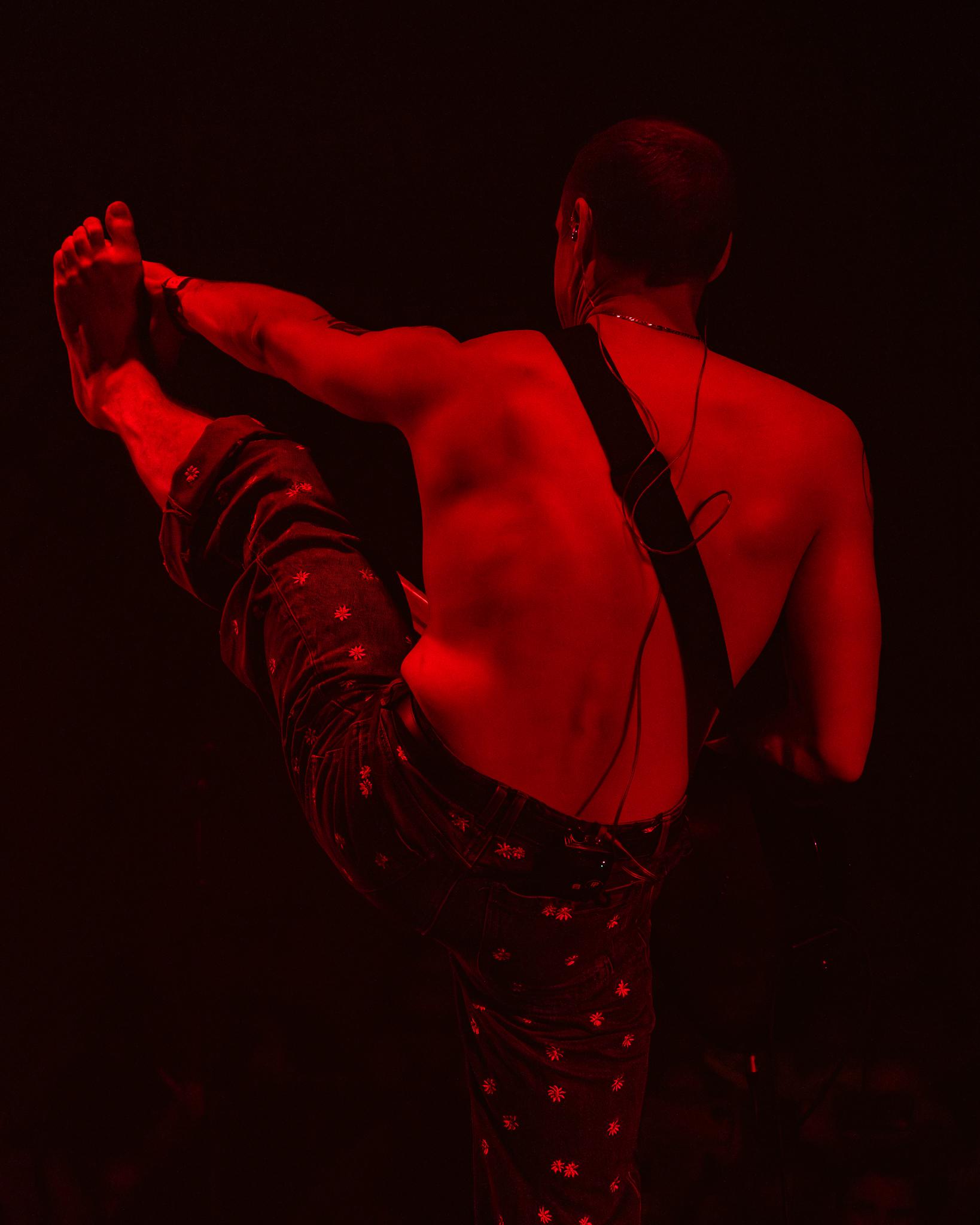 A performer mid high-kick, caught from behind under deep red light
