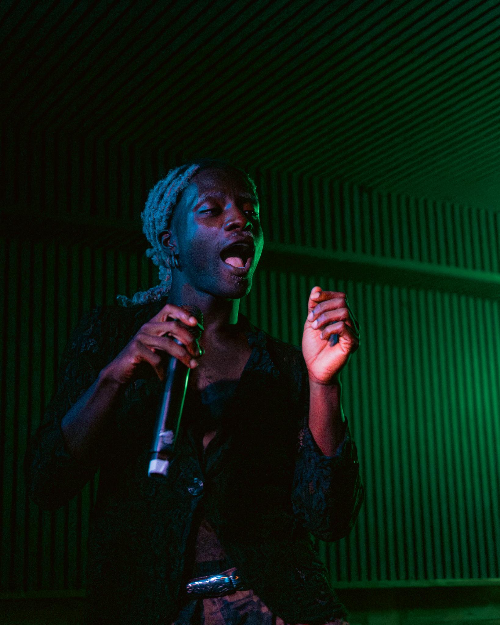 A singer with dreadlocks caught mid-shout under green light, fist raised