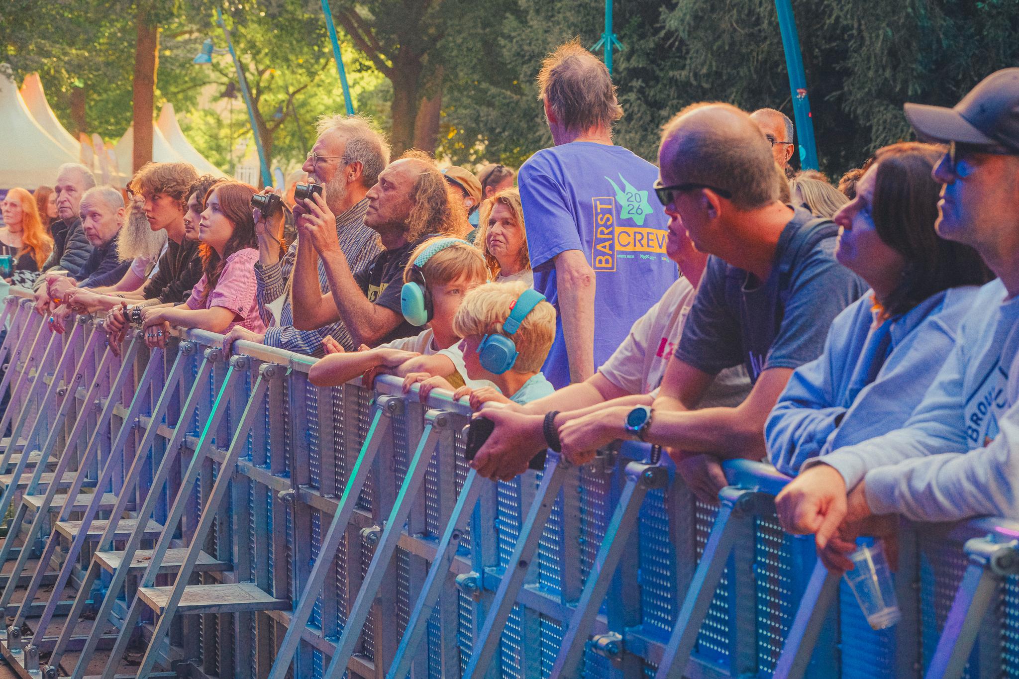 Festival-goers leaning on the barrier, watching the stage in late-day light