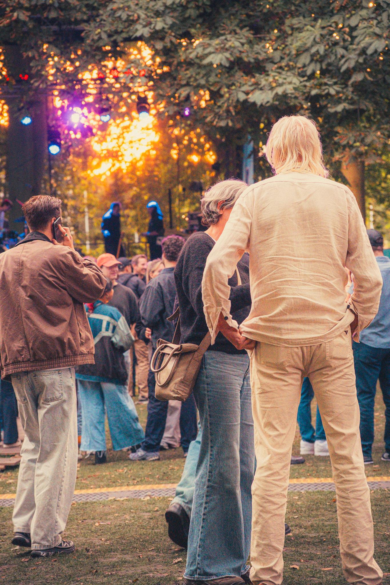A couple watching the stage from the back of a sunlit festival crowd