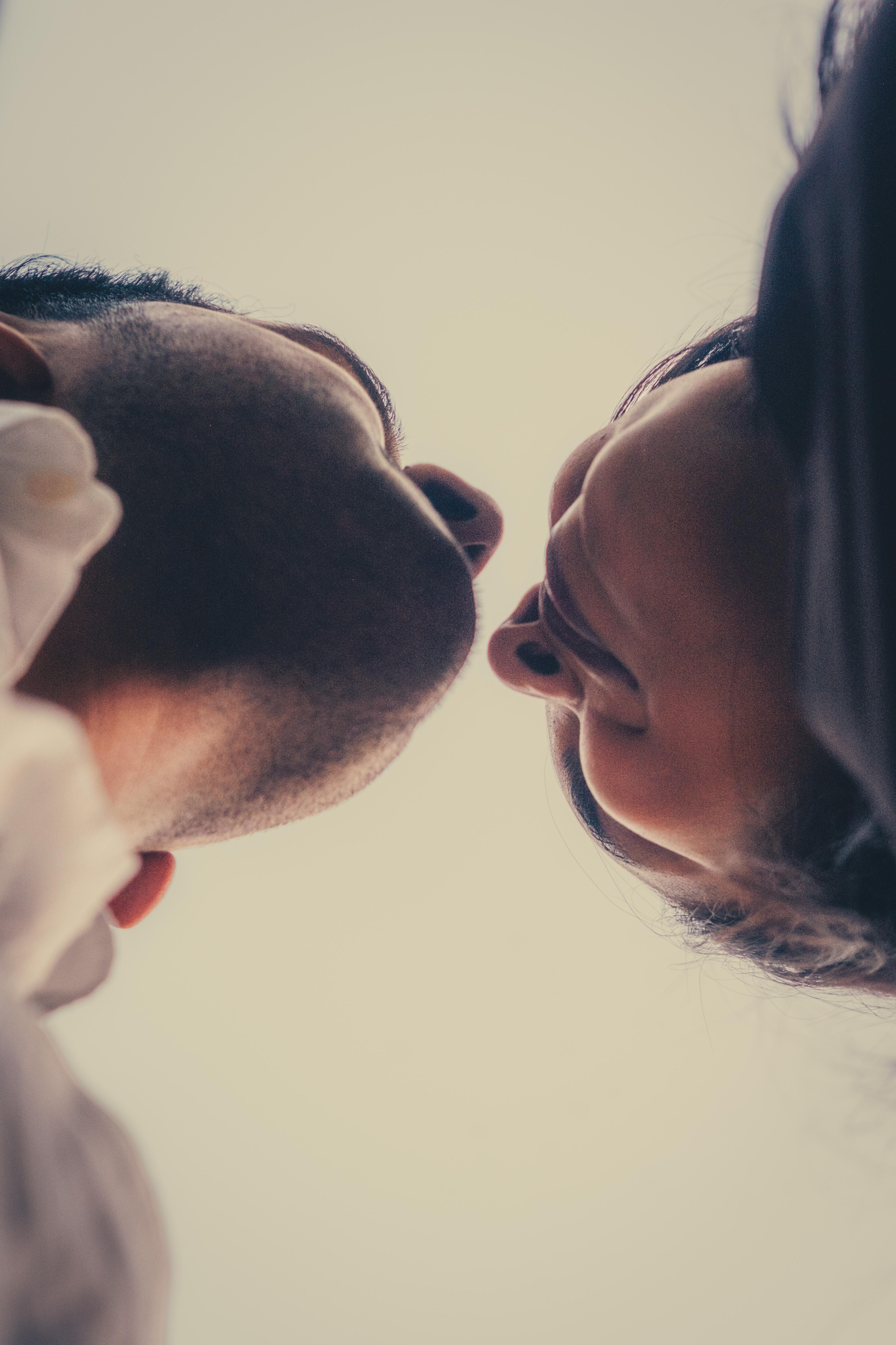 Couple leaning in for a kiss, shot from below against an open sky, lips not quite touching