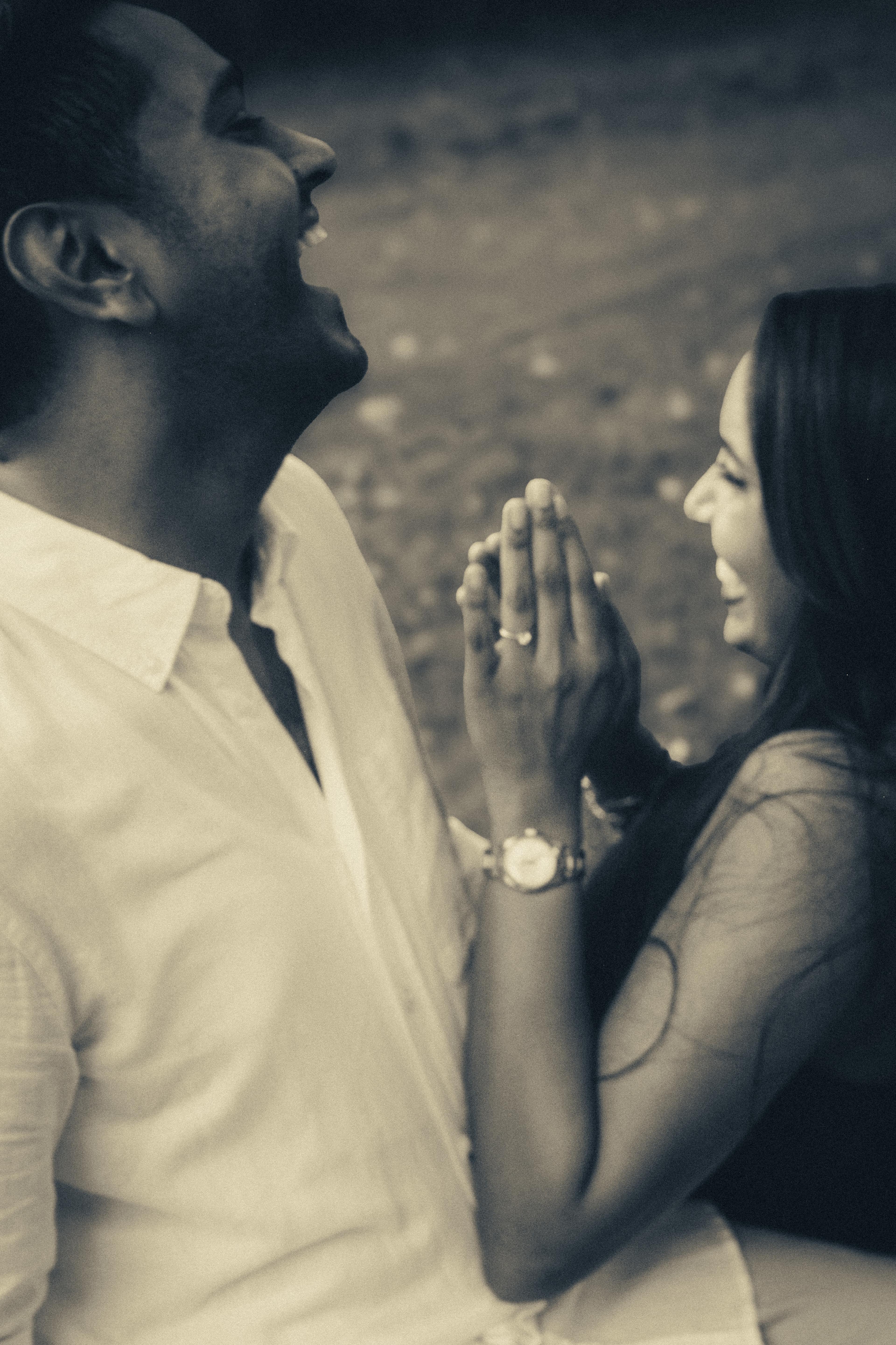 Man laughing with his head tilted back, hands clasped together, while his partner laughs beside him