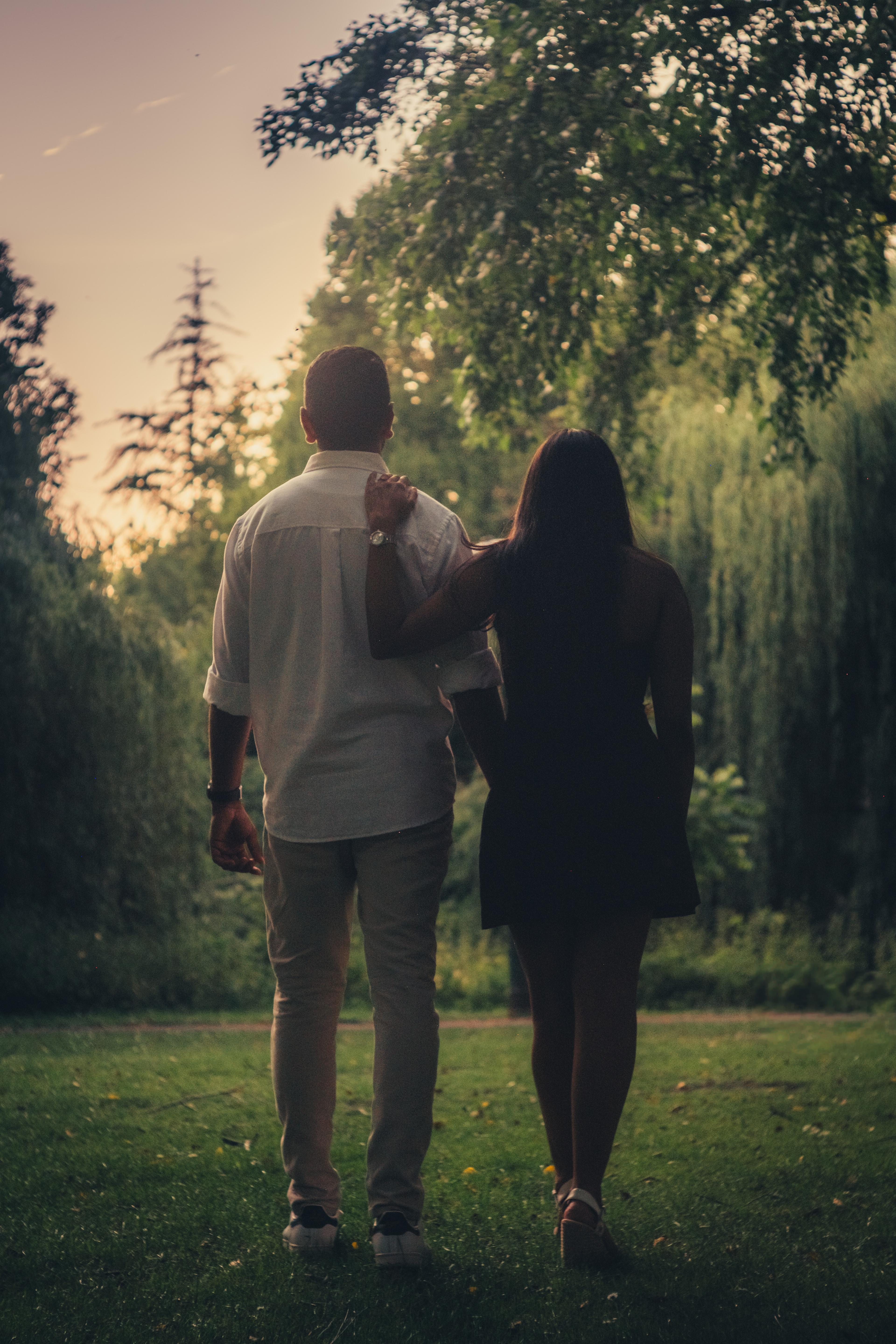 Couple seen from behind, walking through the park, his hand resting on her shoulder