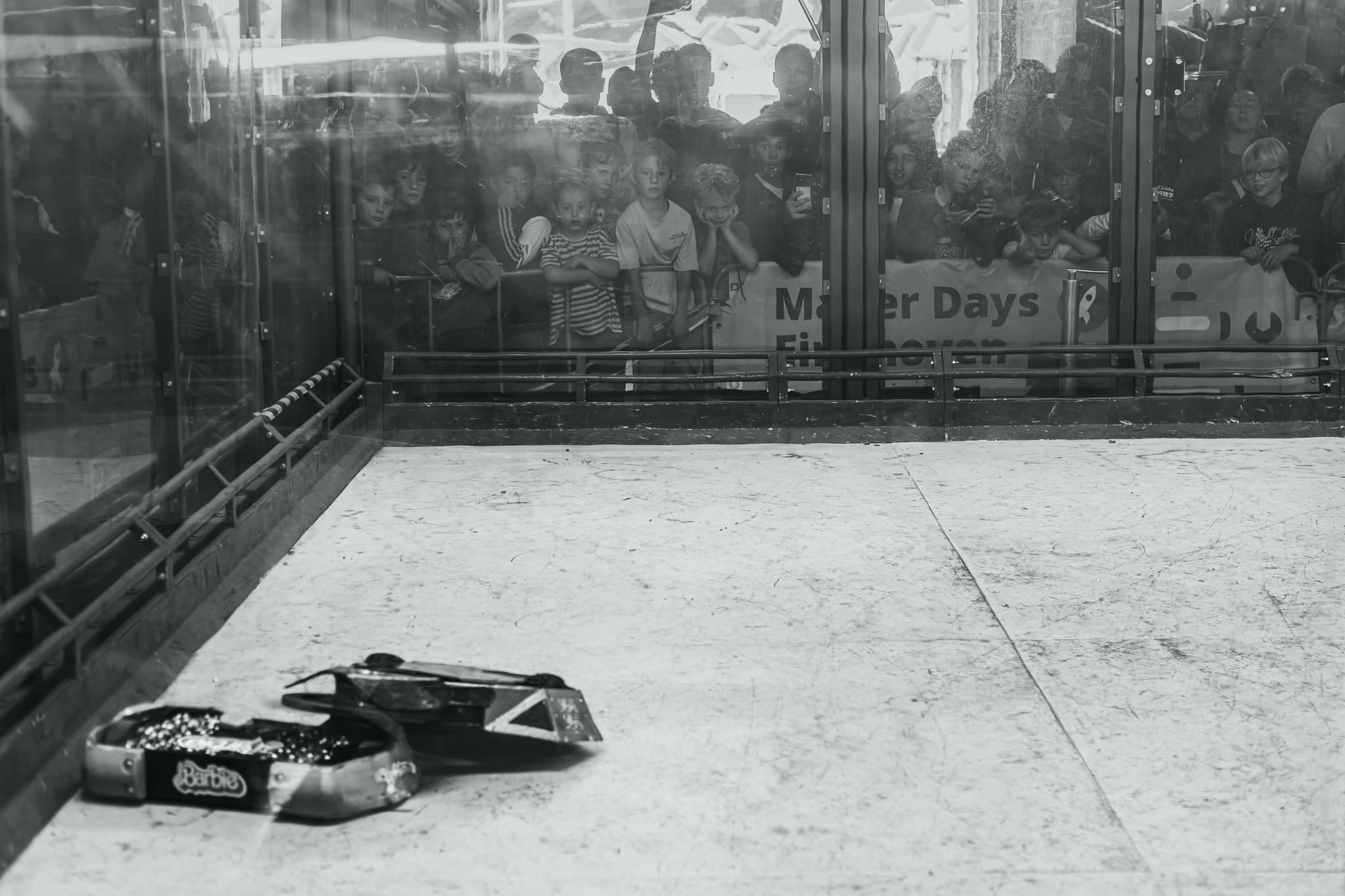 Black-and-white photo of children watching an empty robot battle arena between rounds