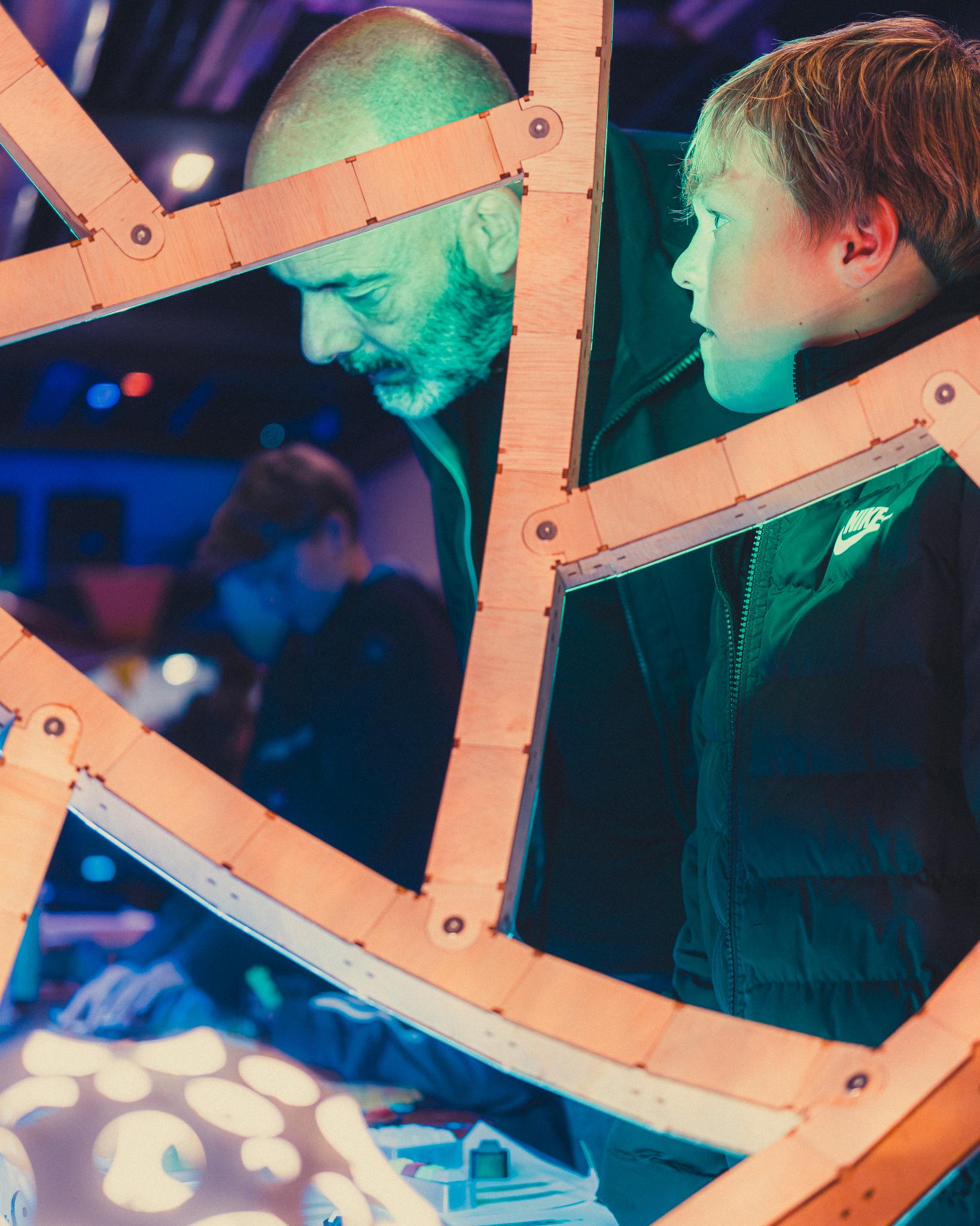 A father and son examining a hands-on exhibit through a wooden frame