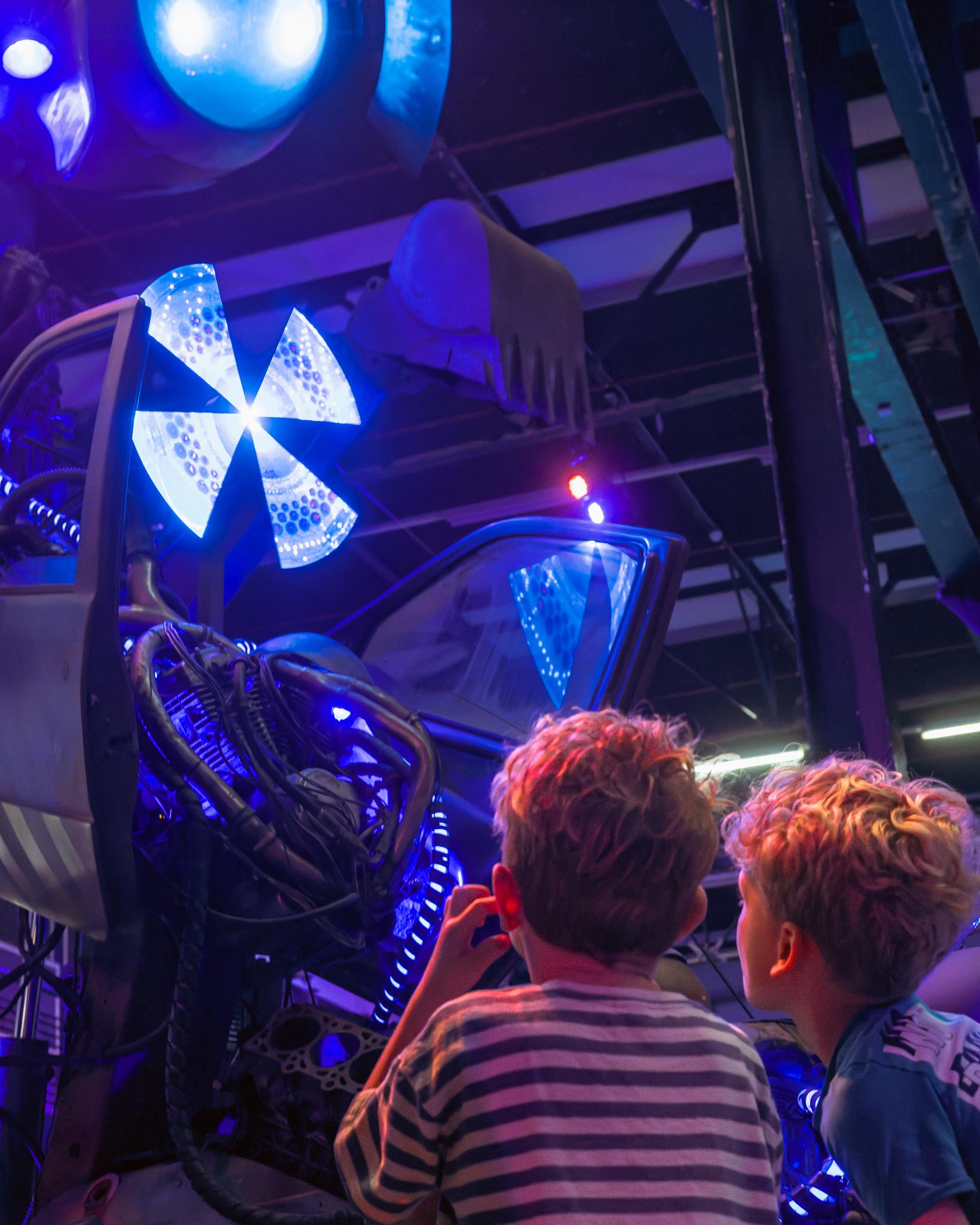 Two children looking up at a glowing blue mechanical exhibit