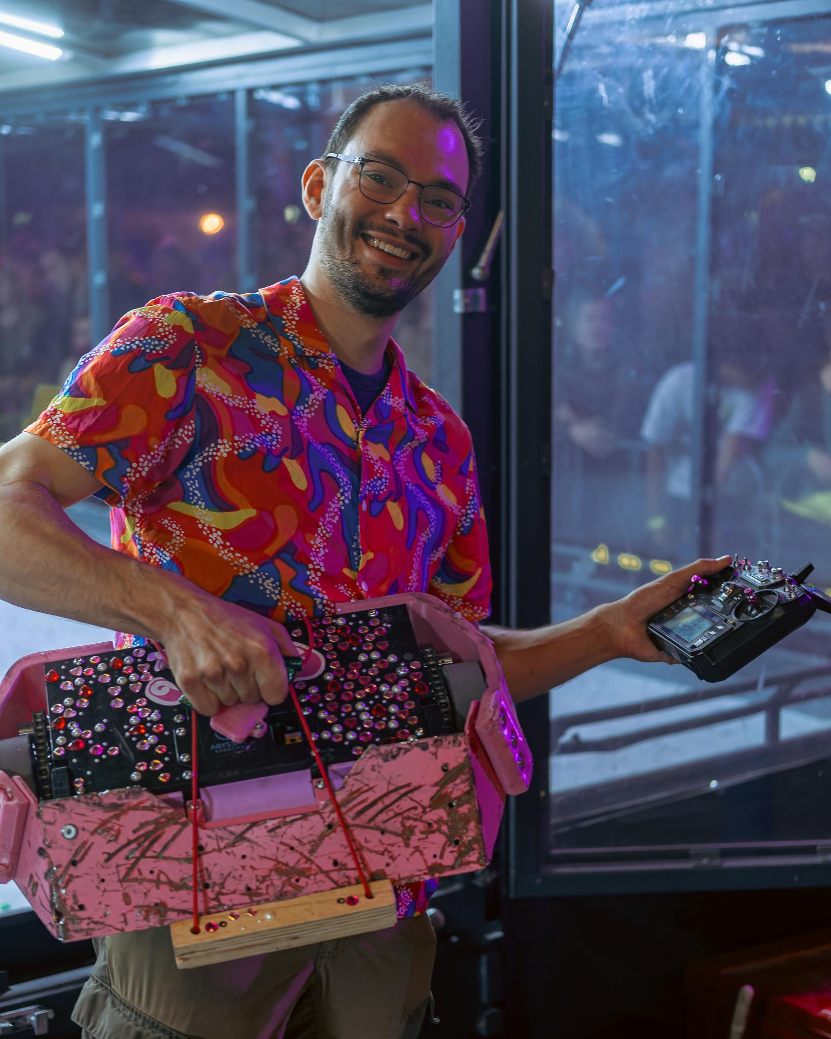 A grinning man in a colorful shirt holding a bejeweled robot and its remote control
