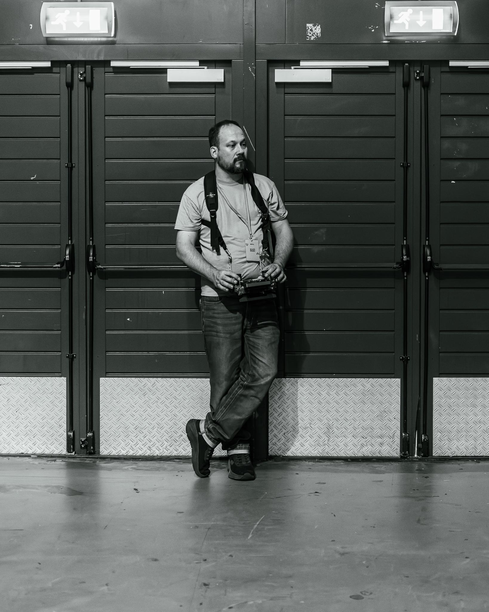 A photographer leaning against a row of shutters between events, in black and white