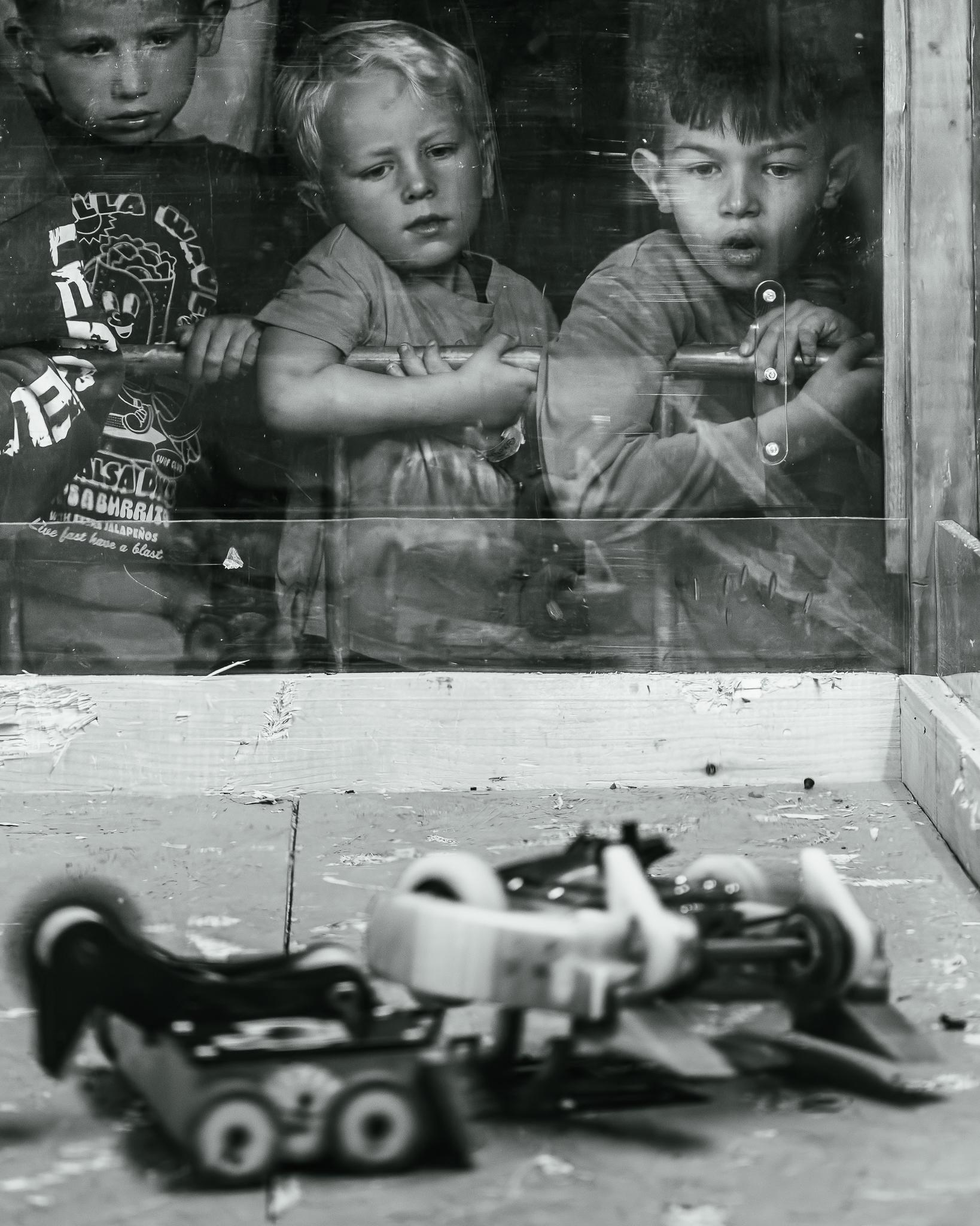 Black-and-white photo of children pressed against a shop window, a toy car blurred in the foreground