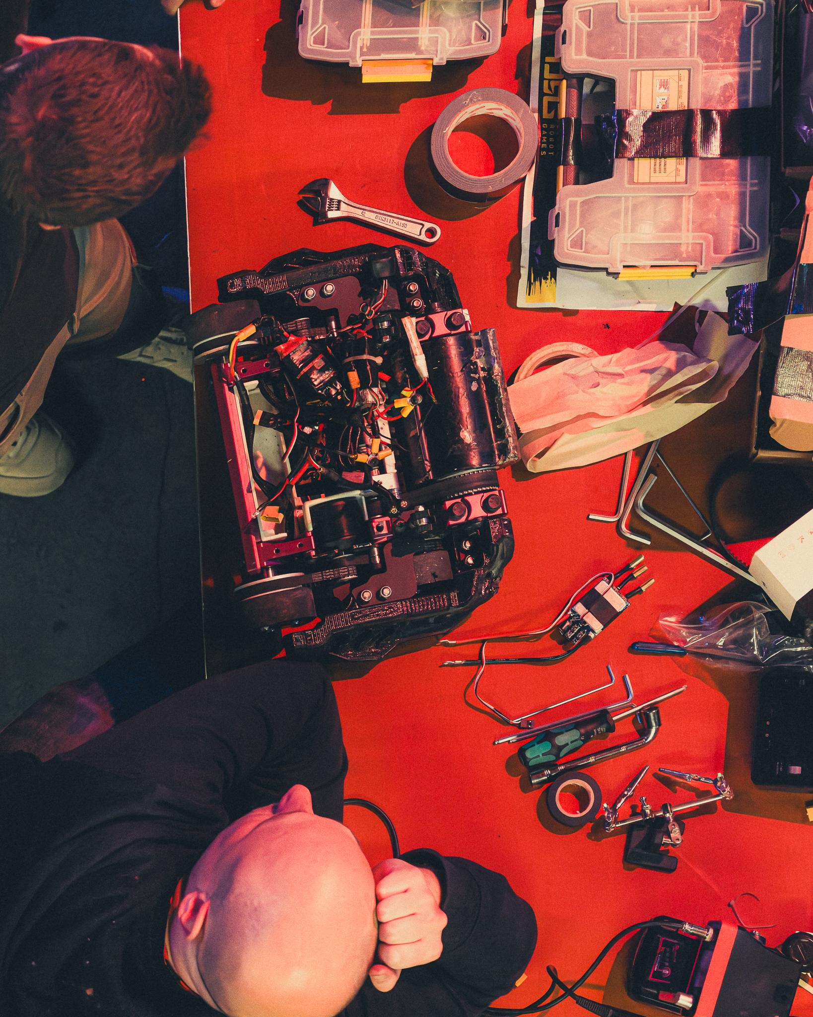 Overhead view of a robotics workshop table, tools and components under red light