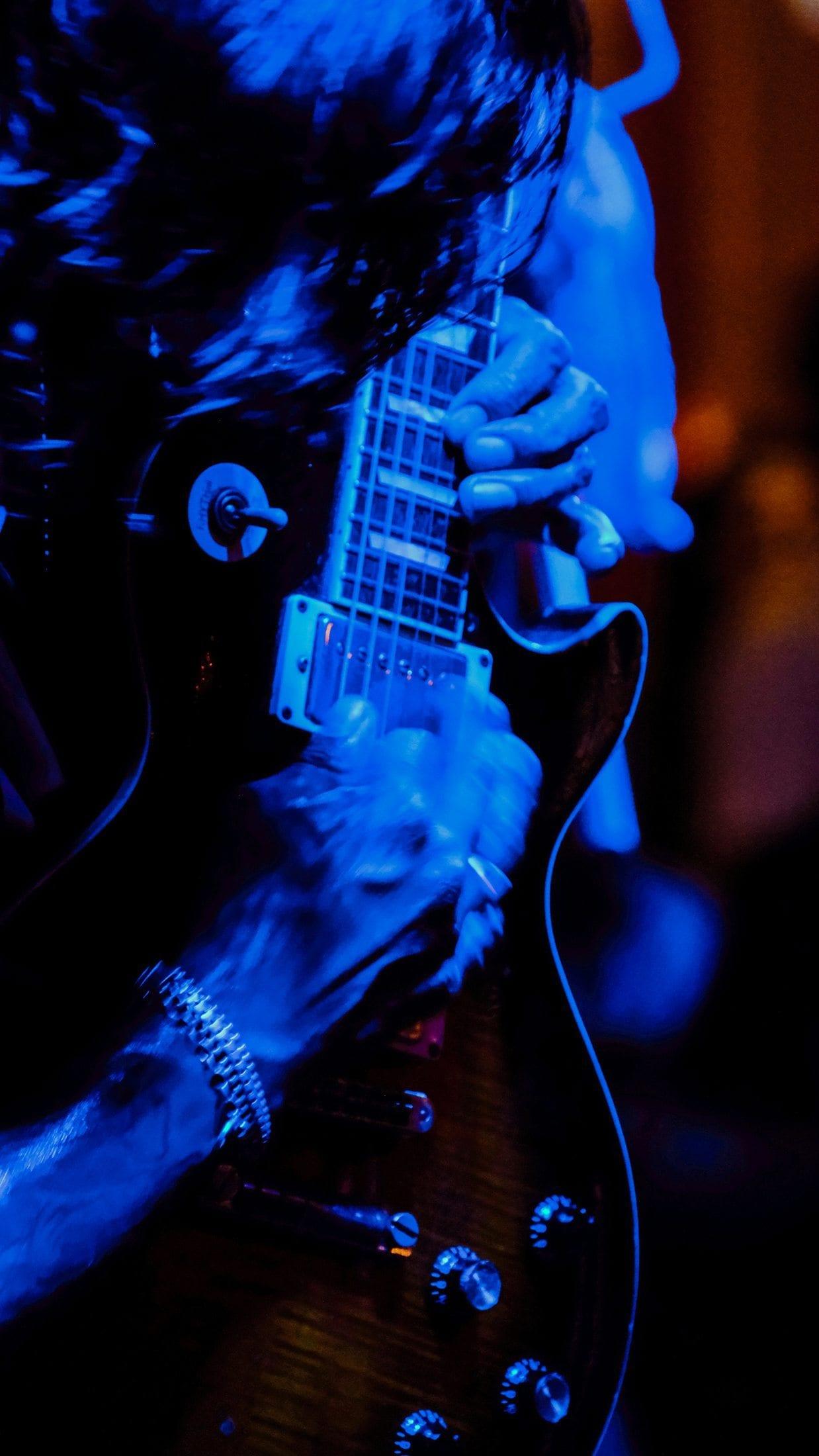 Long exposure of hands moving across an electric guitar in blue light